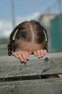 A young girl peeking over a wooden fence