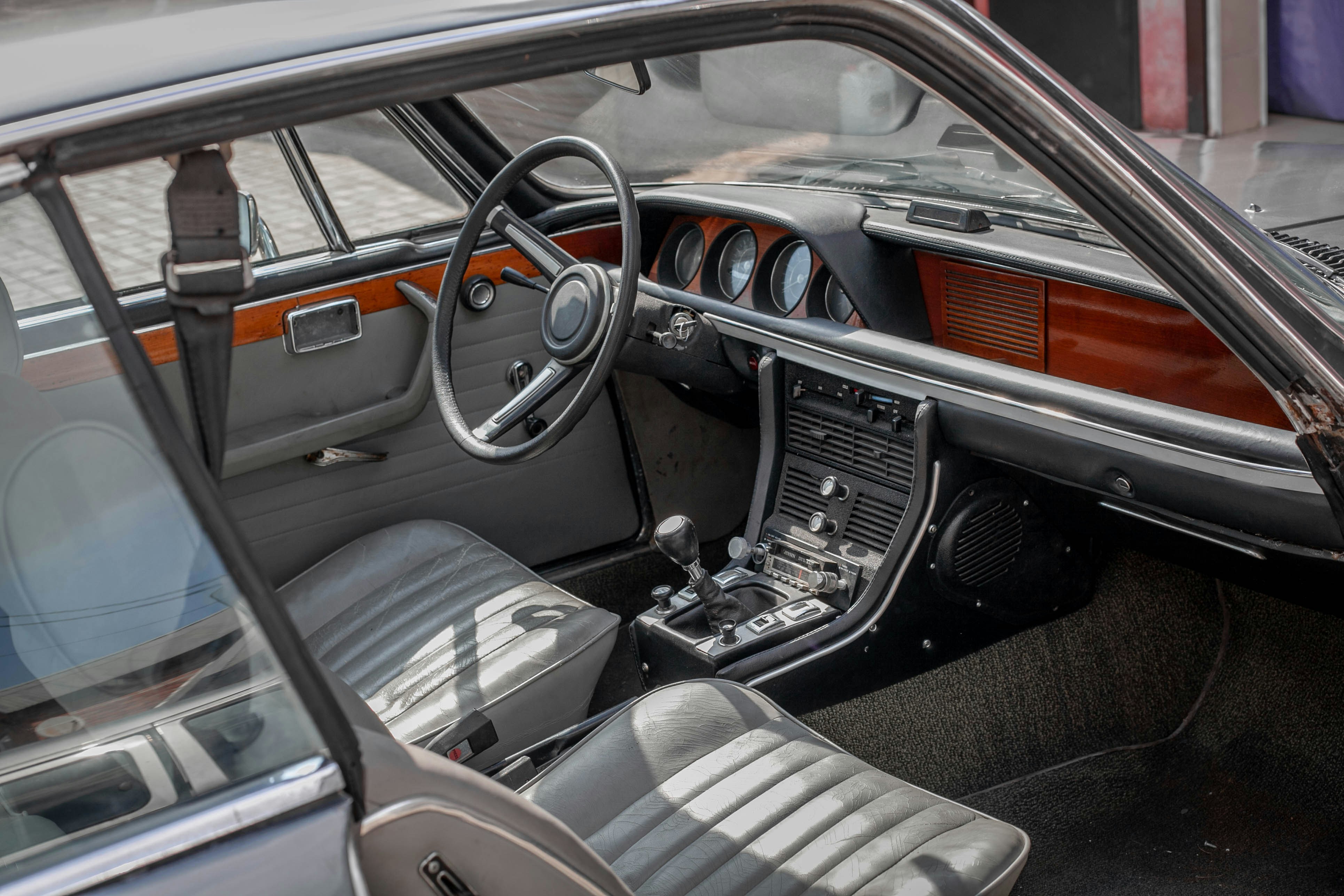 Abitacolo auto d'epoca con volante, cruscotto e sedili grigi.