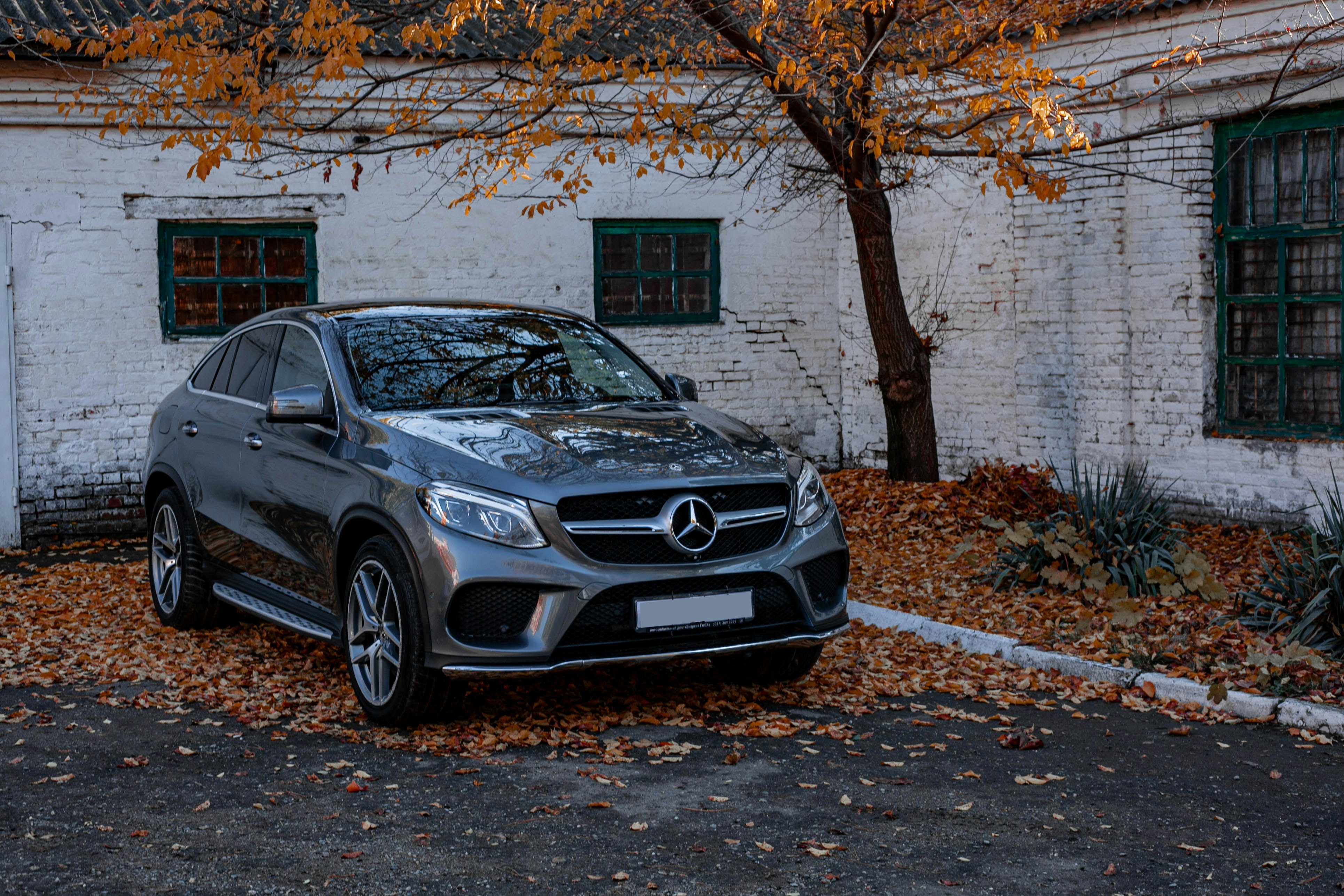 SUV grigio Mercedes-Benz parcheggiato accanto a un edificio con foglie autunnali.