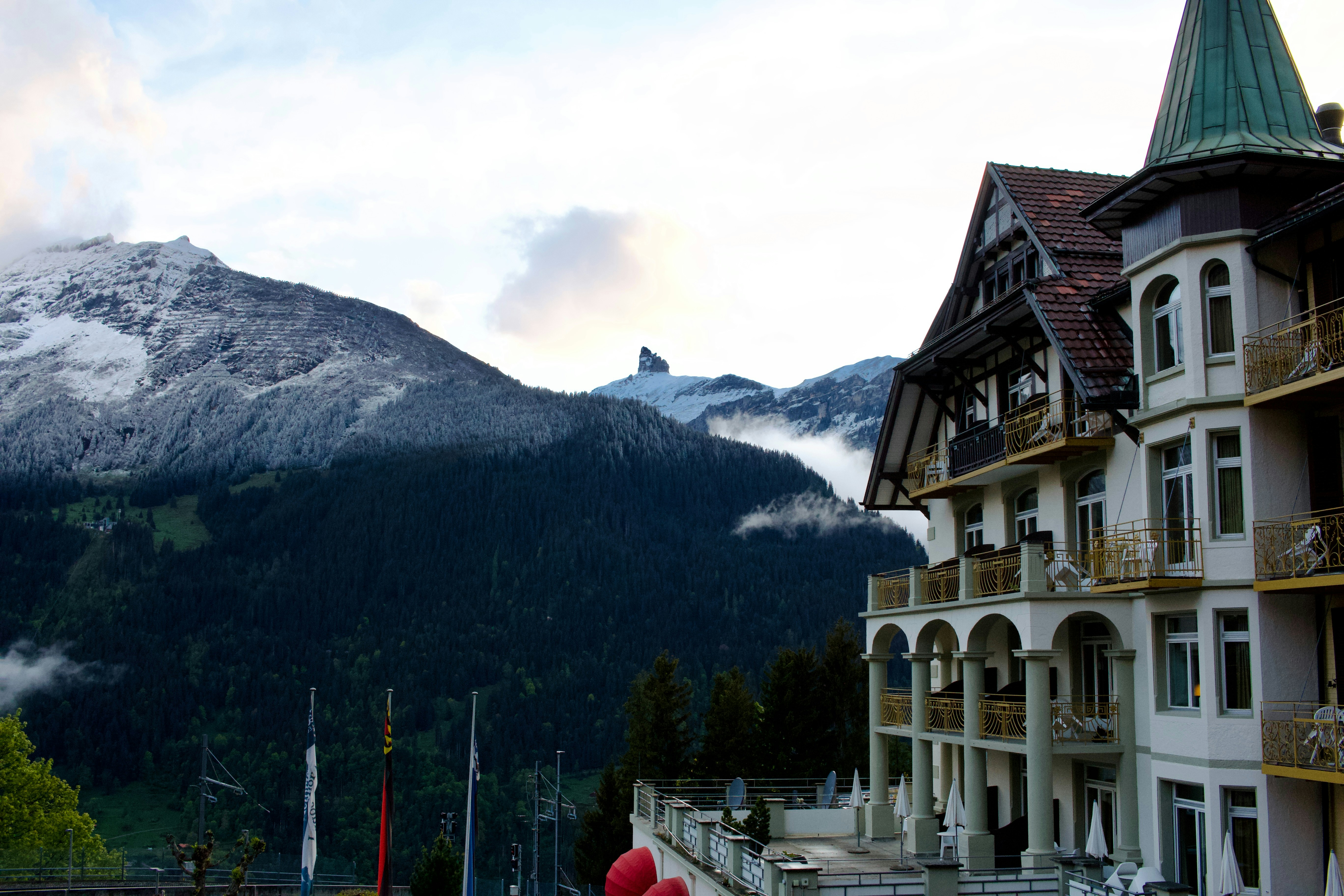 Ornate hotel building with snow-capped mountains and forests in background.