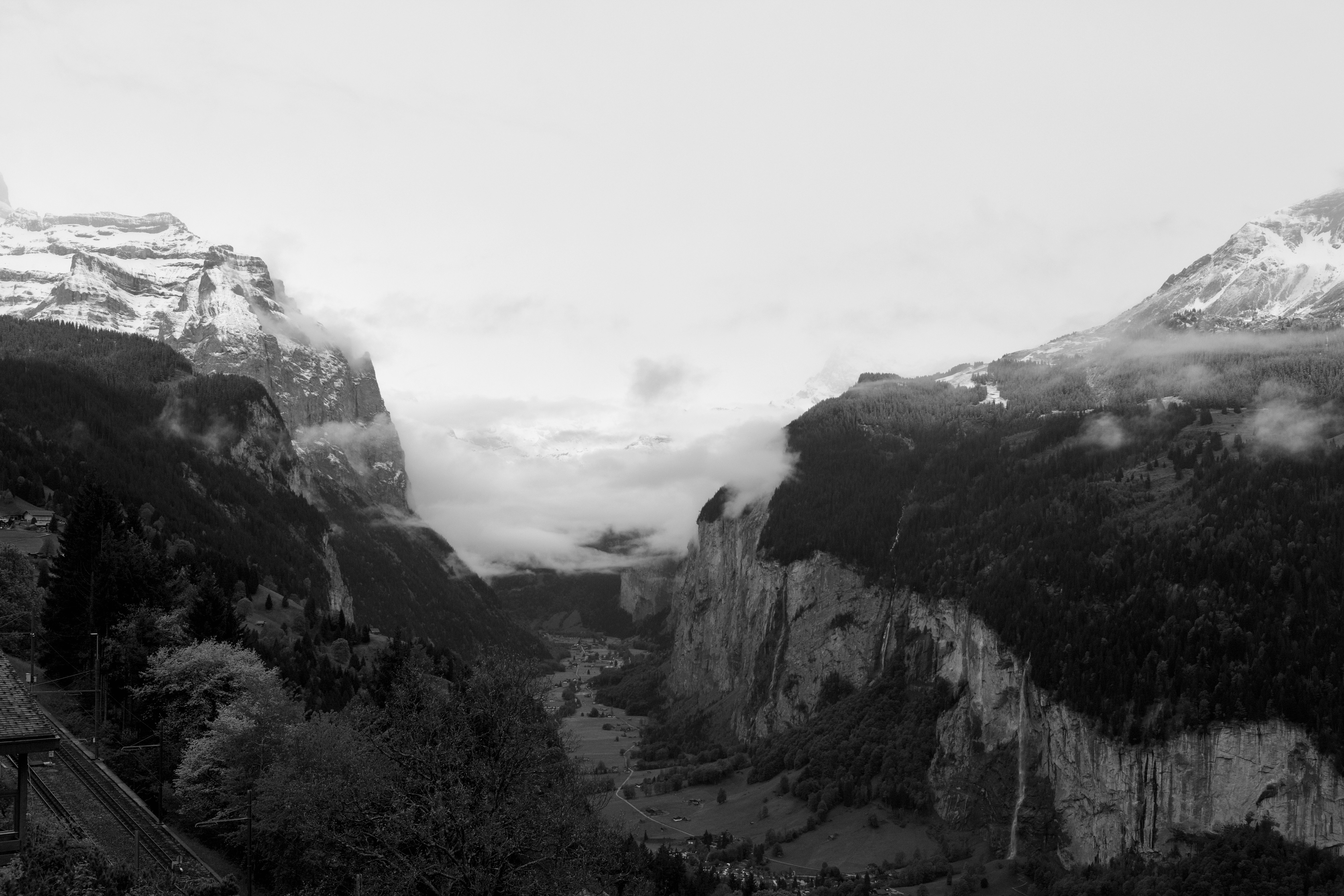 Misty valley between snow-capped mountains in black and white.