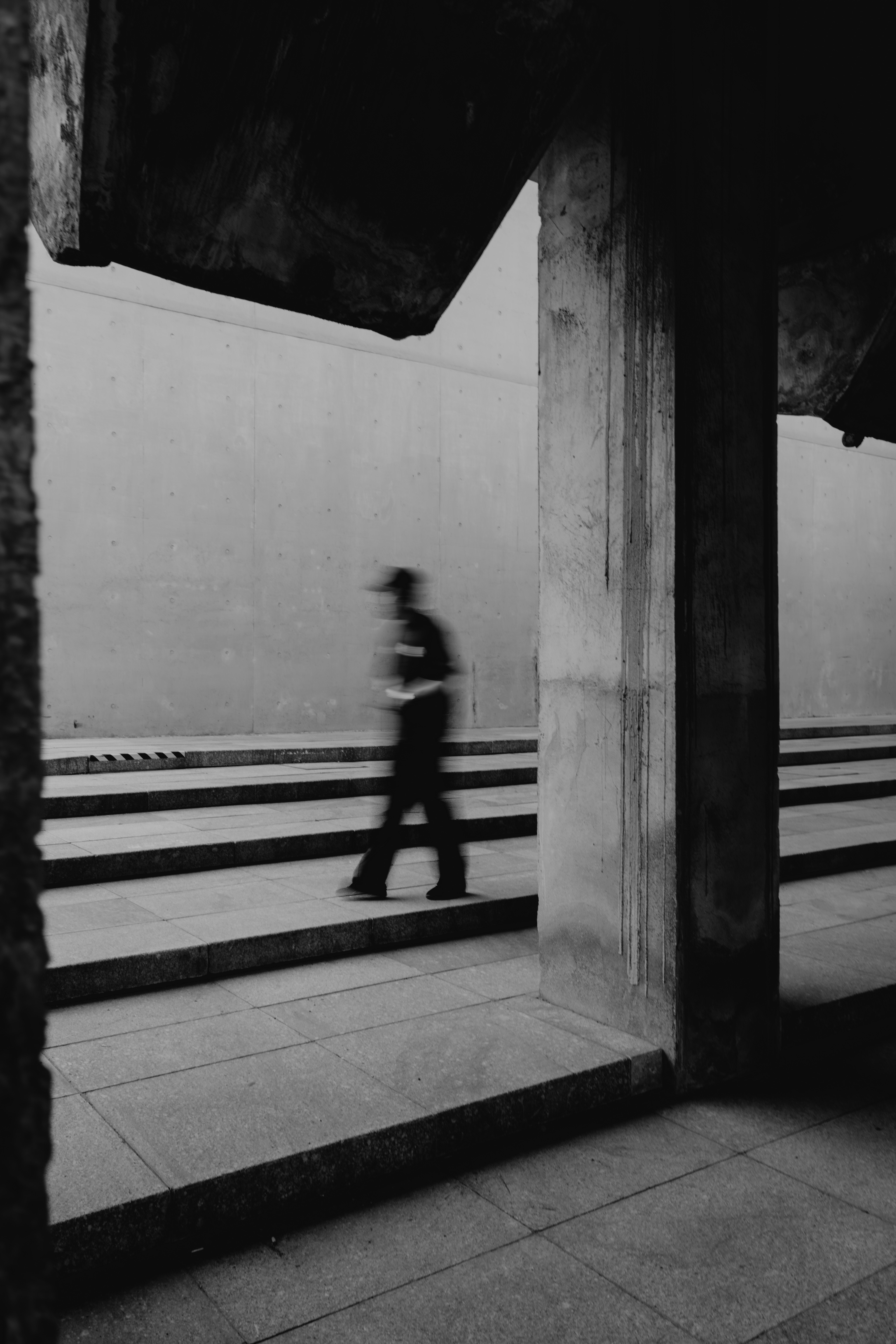 Blurred person walks through a minimalist concrete passage.