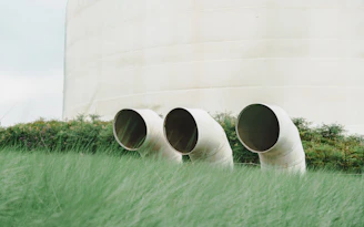 Three large pipes emerge from green grass near a building.