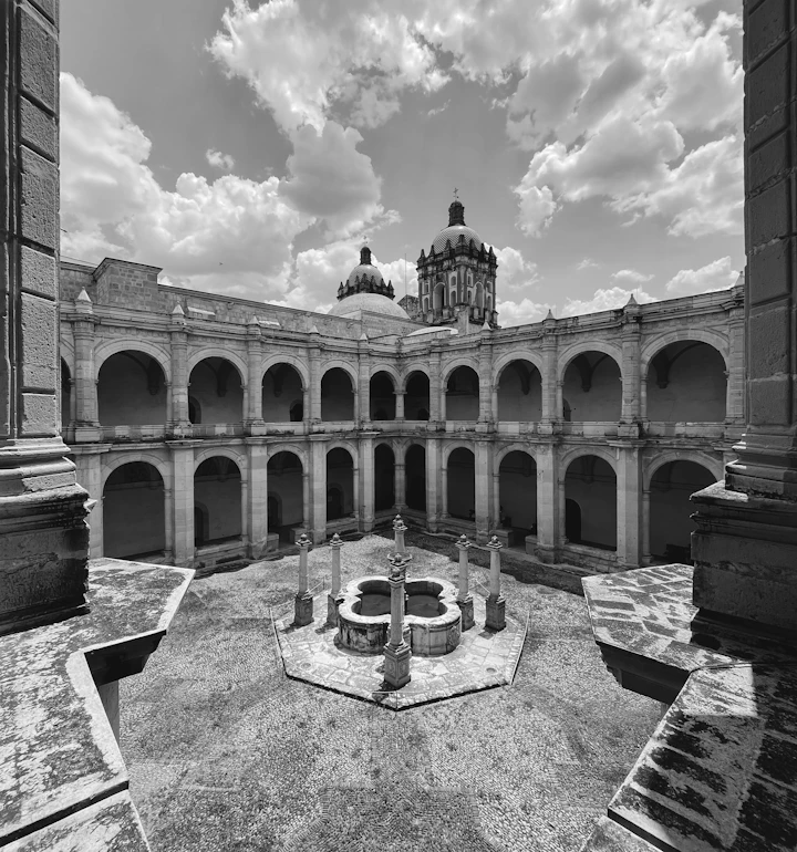 Patio colonial con fuente central y arcadas de piedra al atardecer