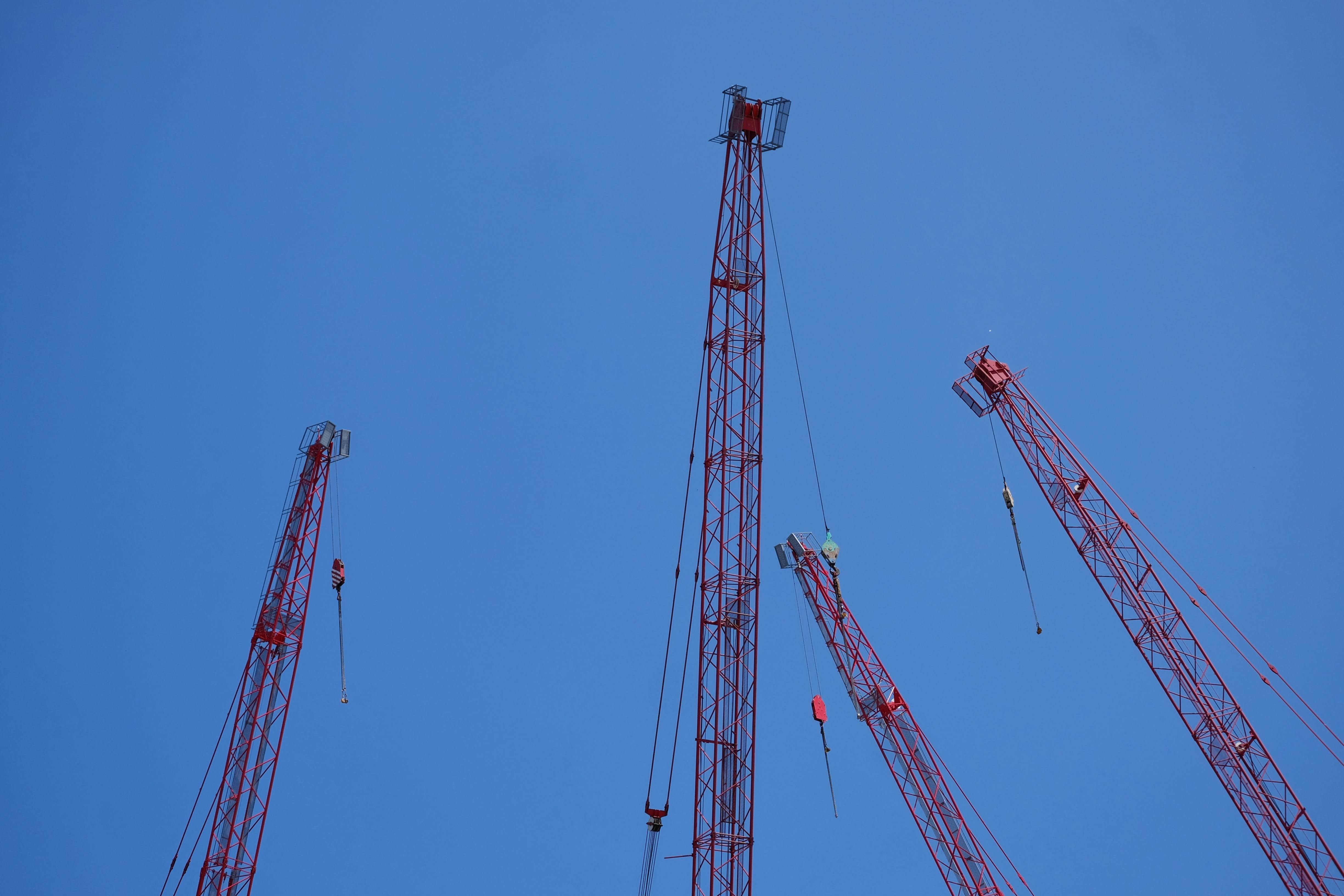 Grúas de construcción rojas contra un cielo azul despejado.