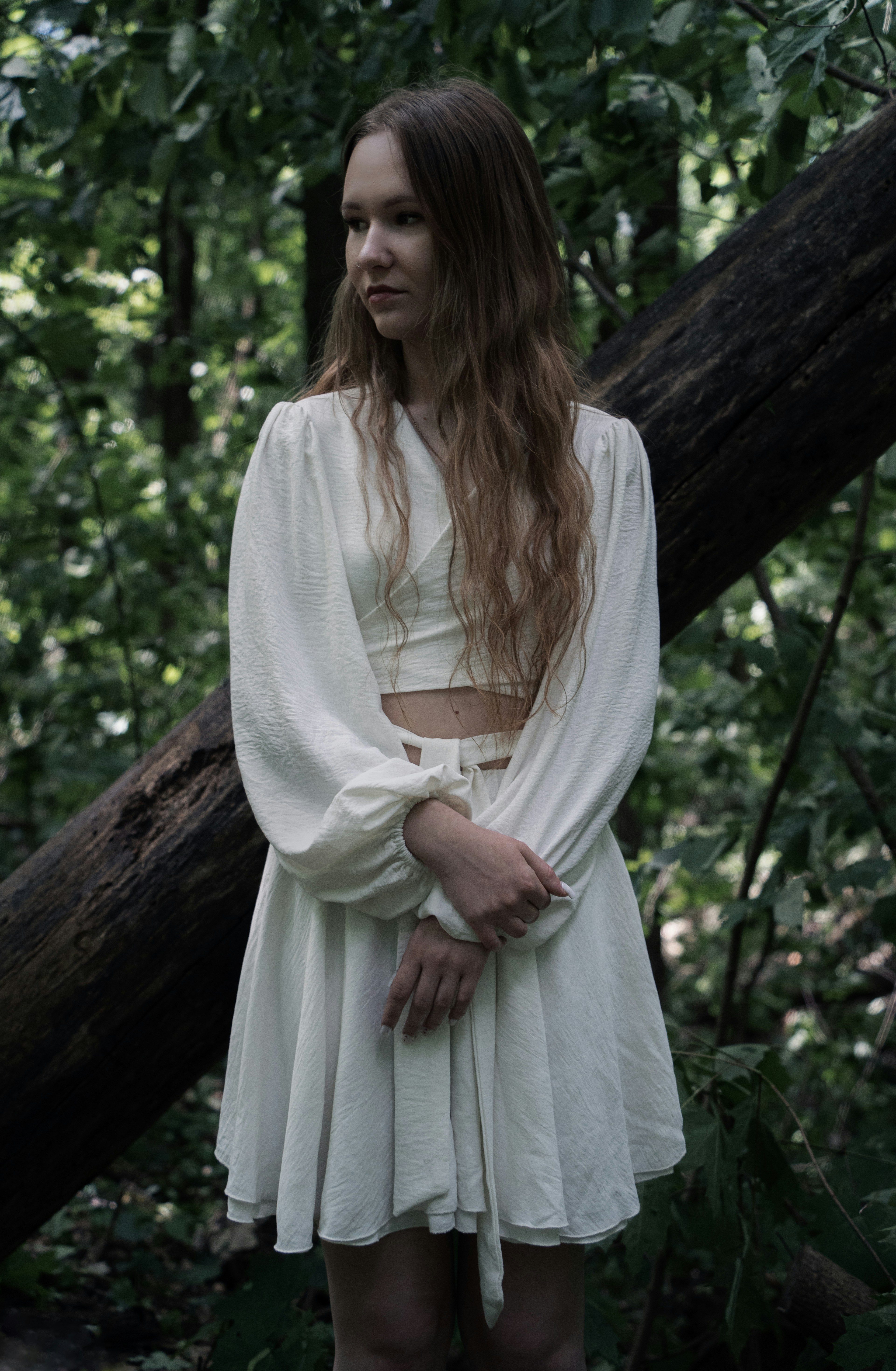 A young woman in white stands in a dark forest.