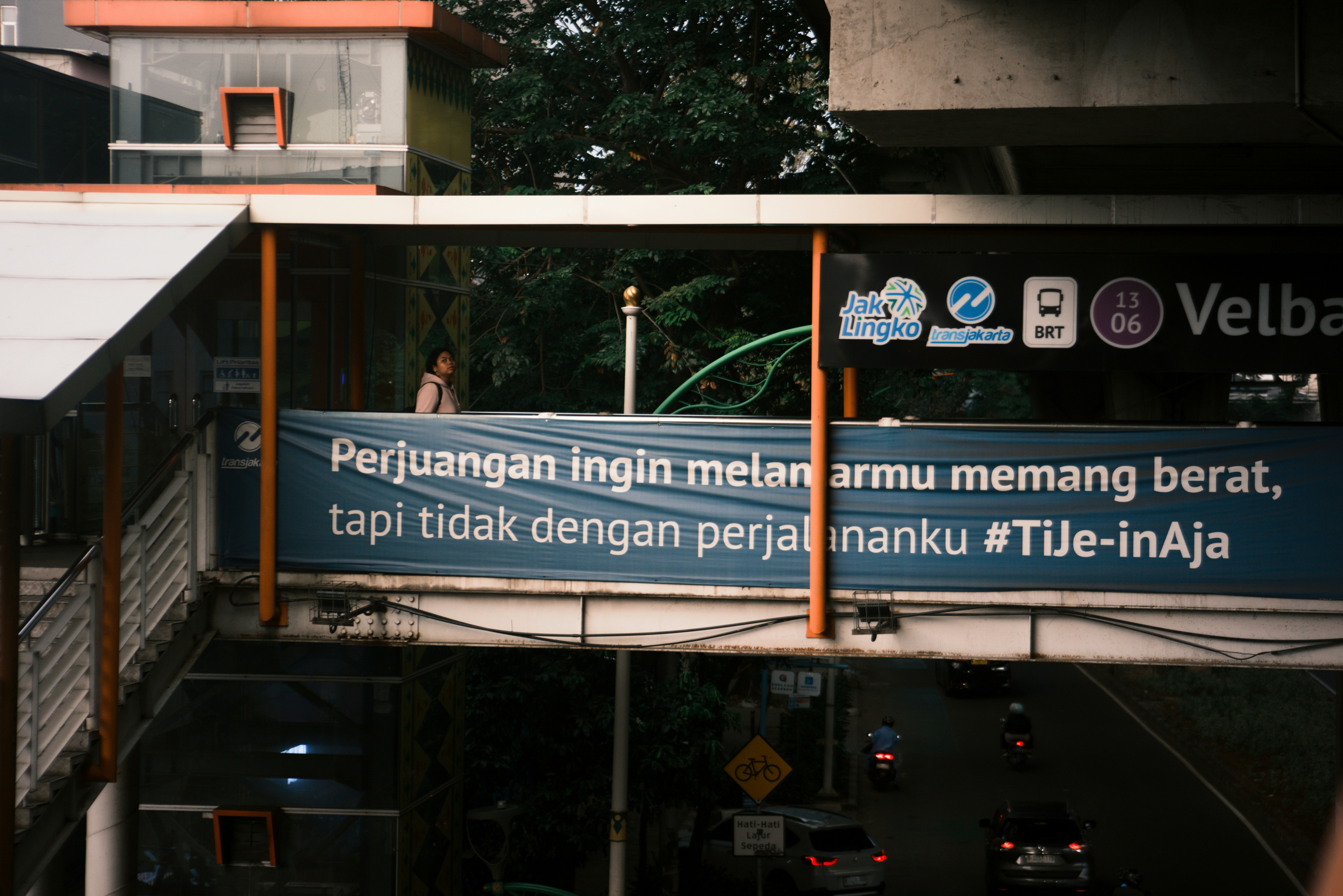 Jembatan penyeberangan dengan spanduk di atas jalan yang sibuk.