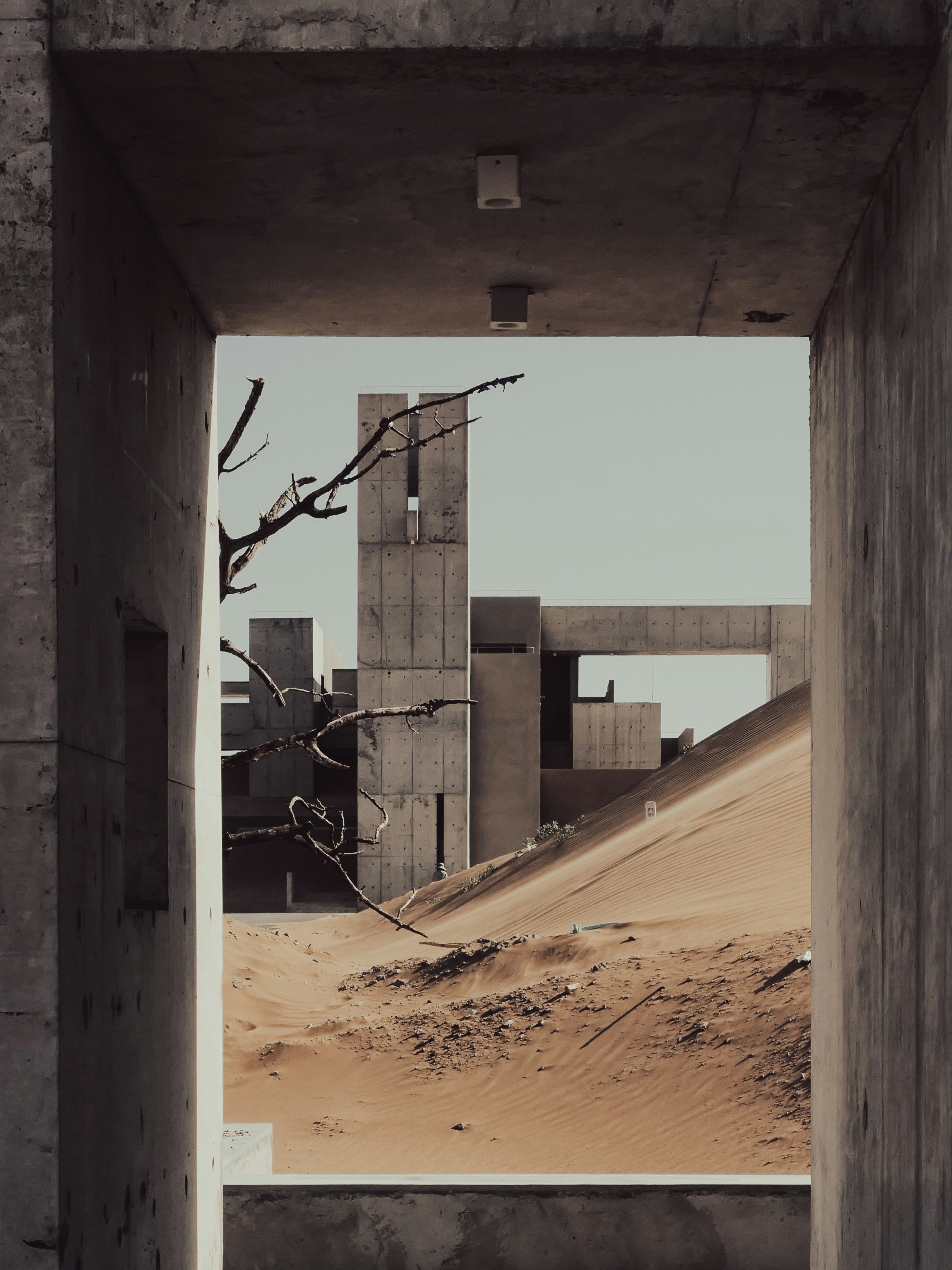 Brutalist concrete buildings rise from sand dunes in the desert.