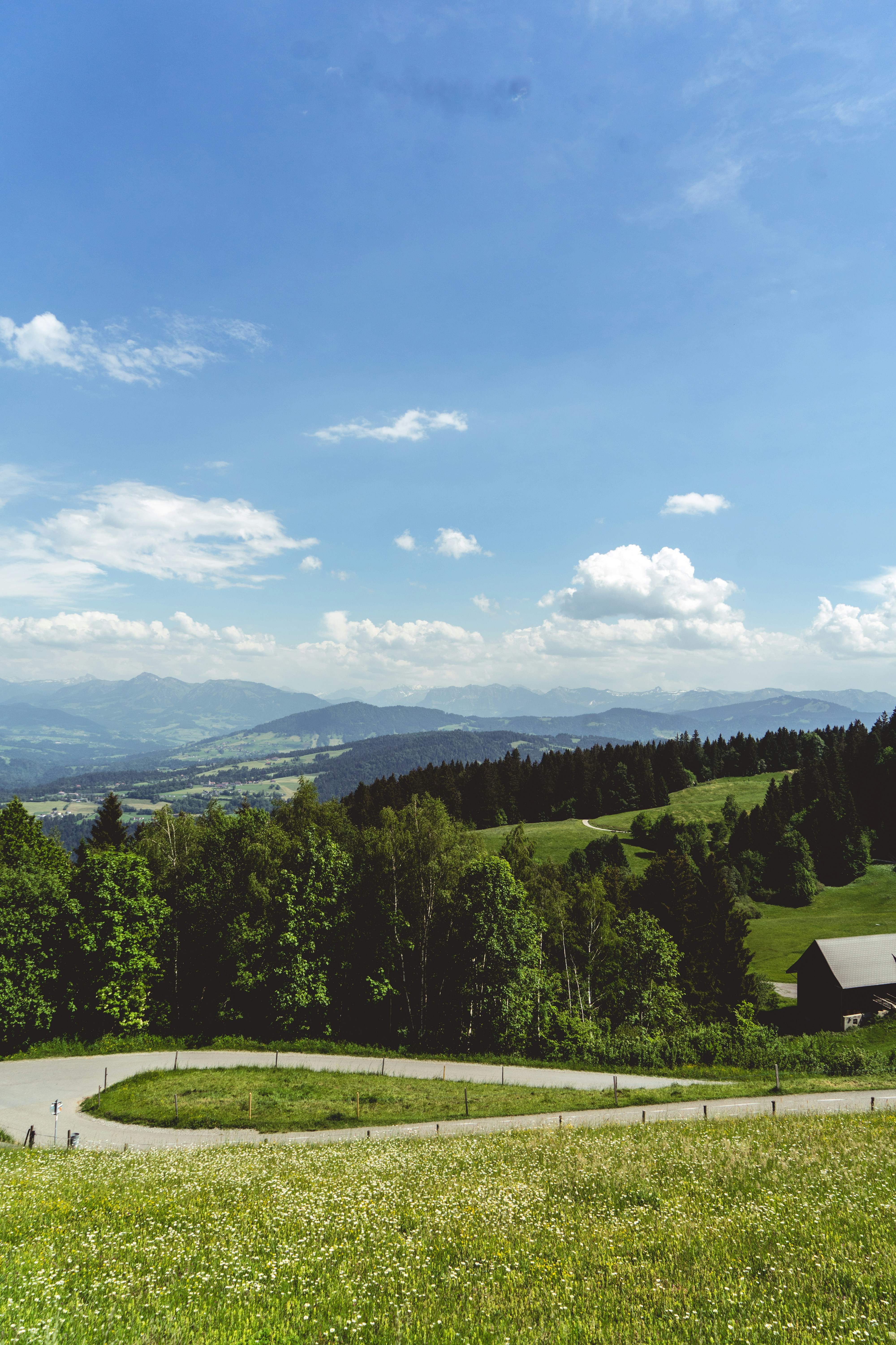 Winding road through green hills, distant mountains, and blue sky.