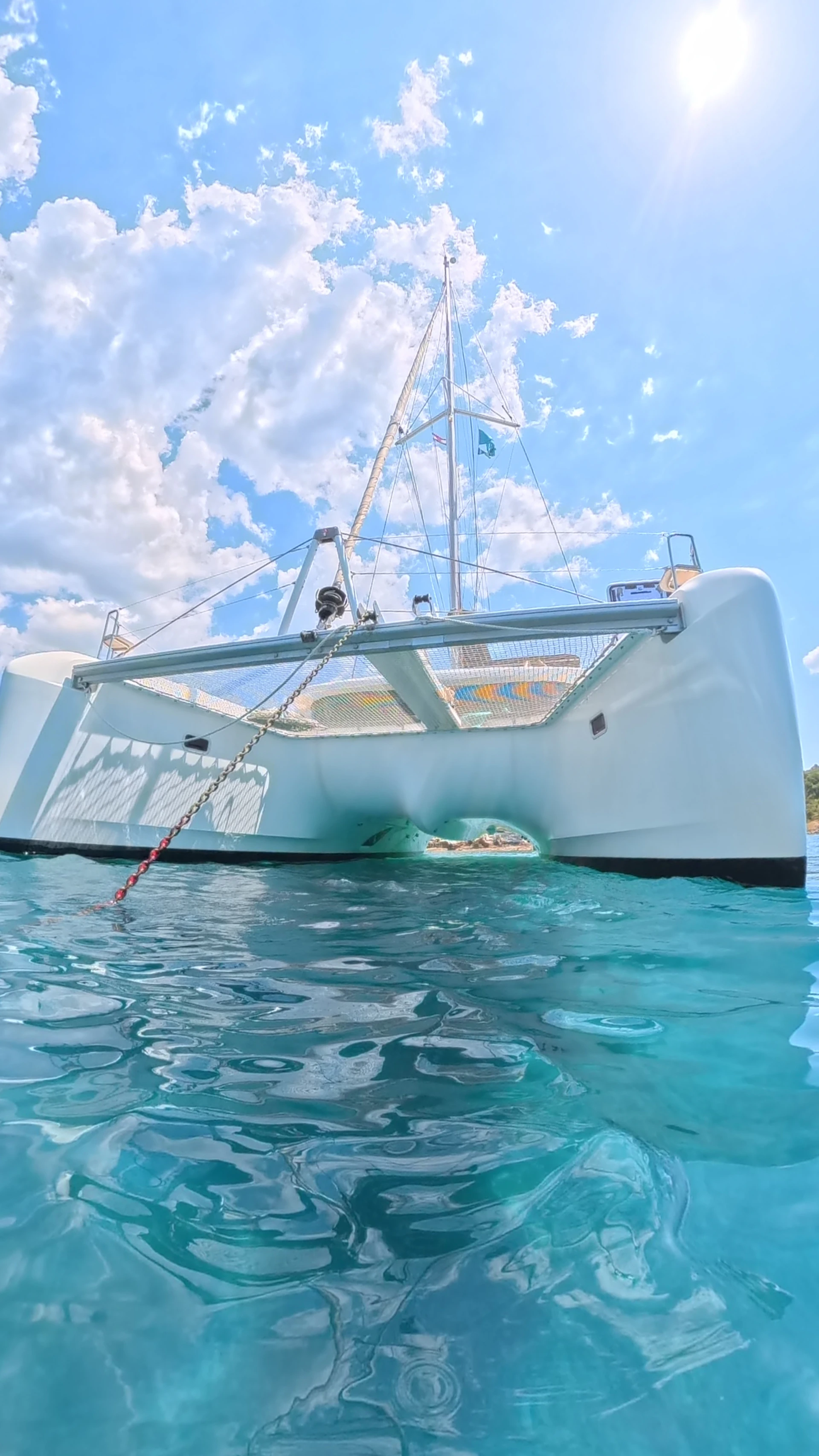 White catamaran floating in clear turquoise water under sunny sky.