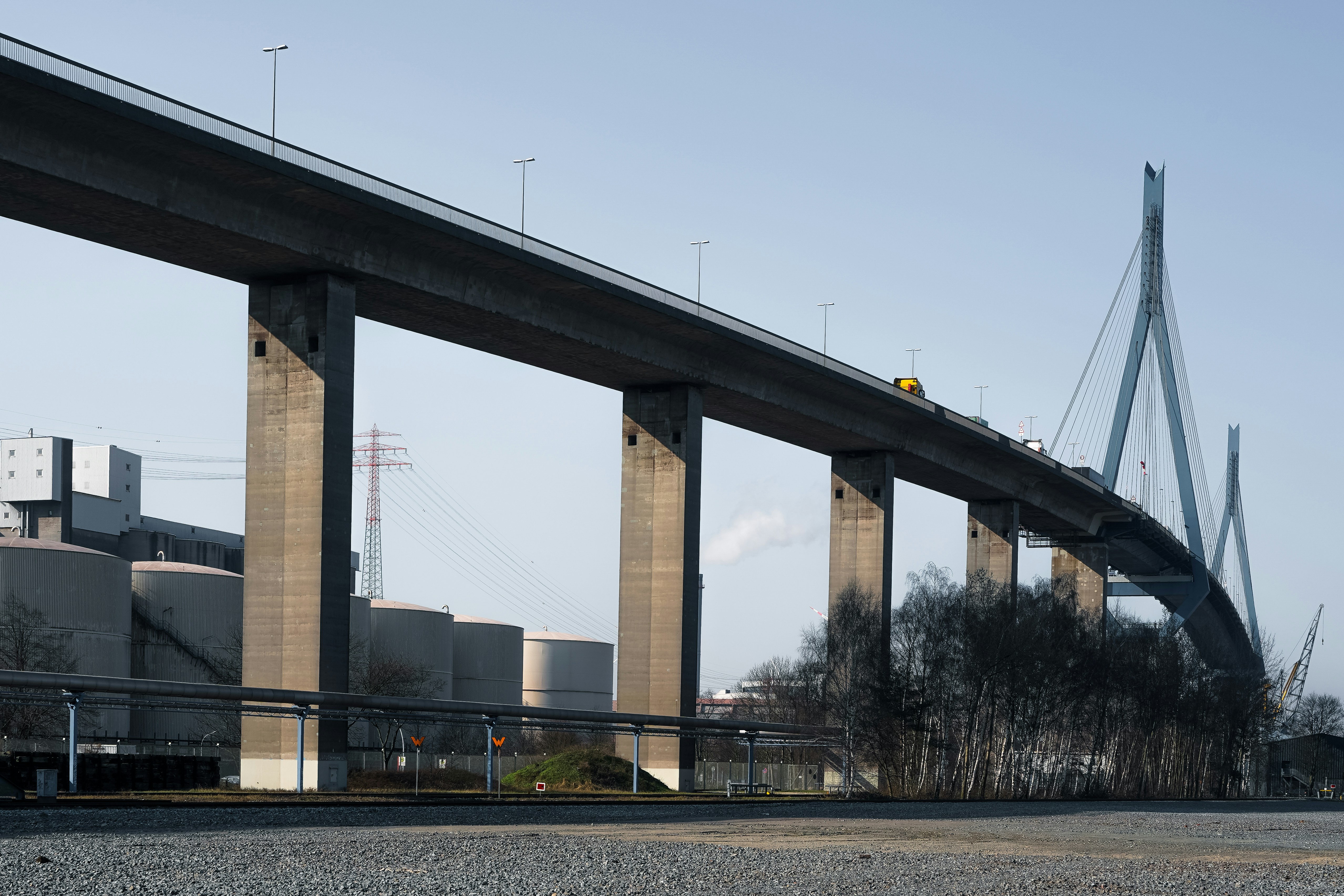 Jembatan jalan raya beton dengan latar belakang industri dan pepohonan gundul.