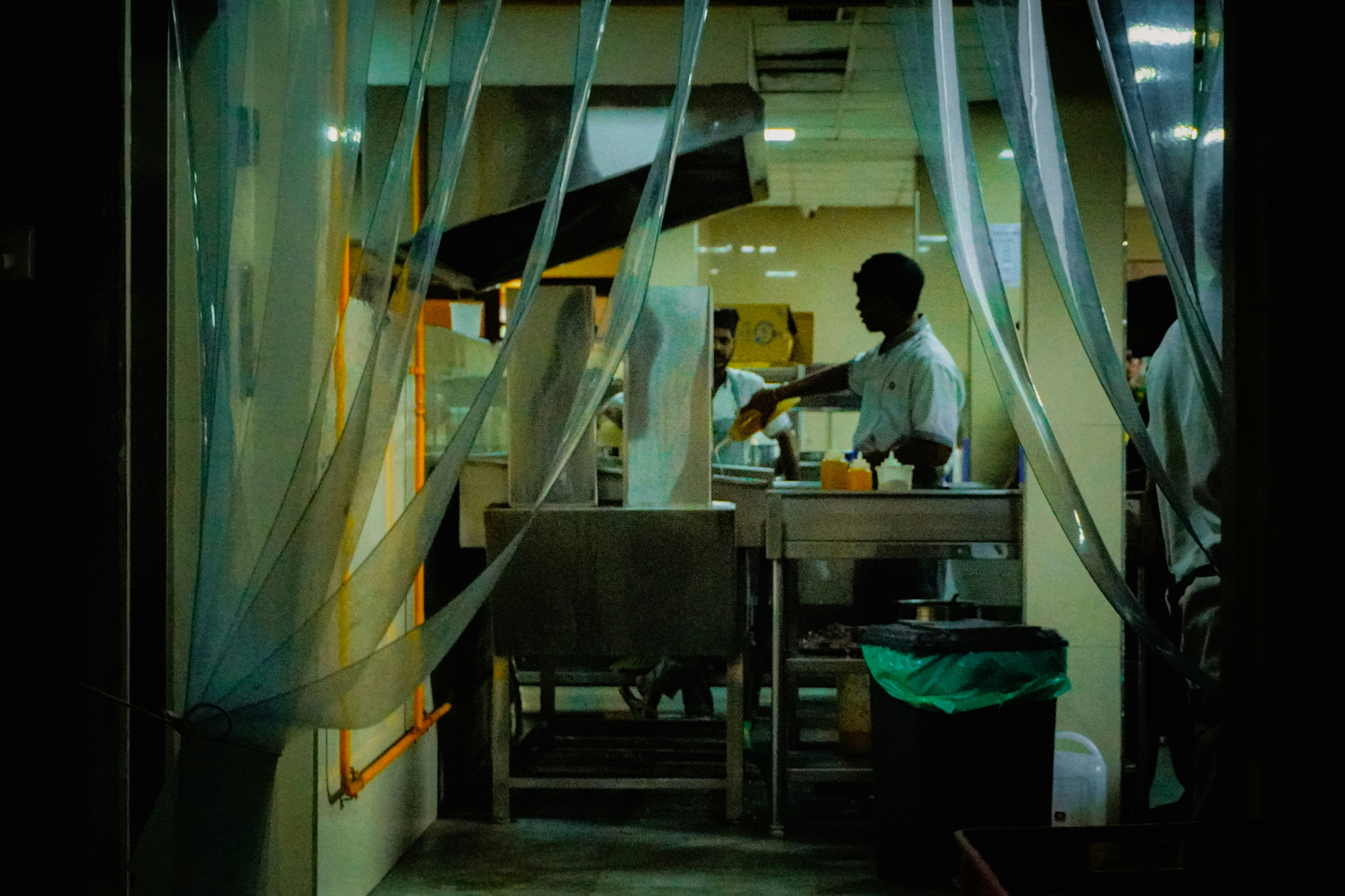 A chef working in a kitchen seen through plastic strips.