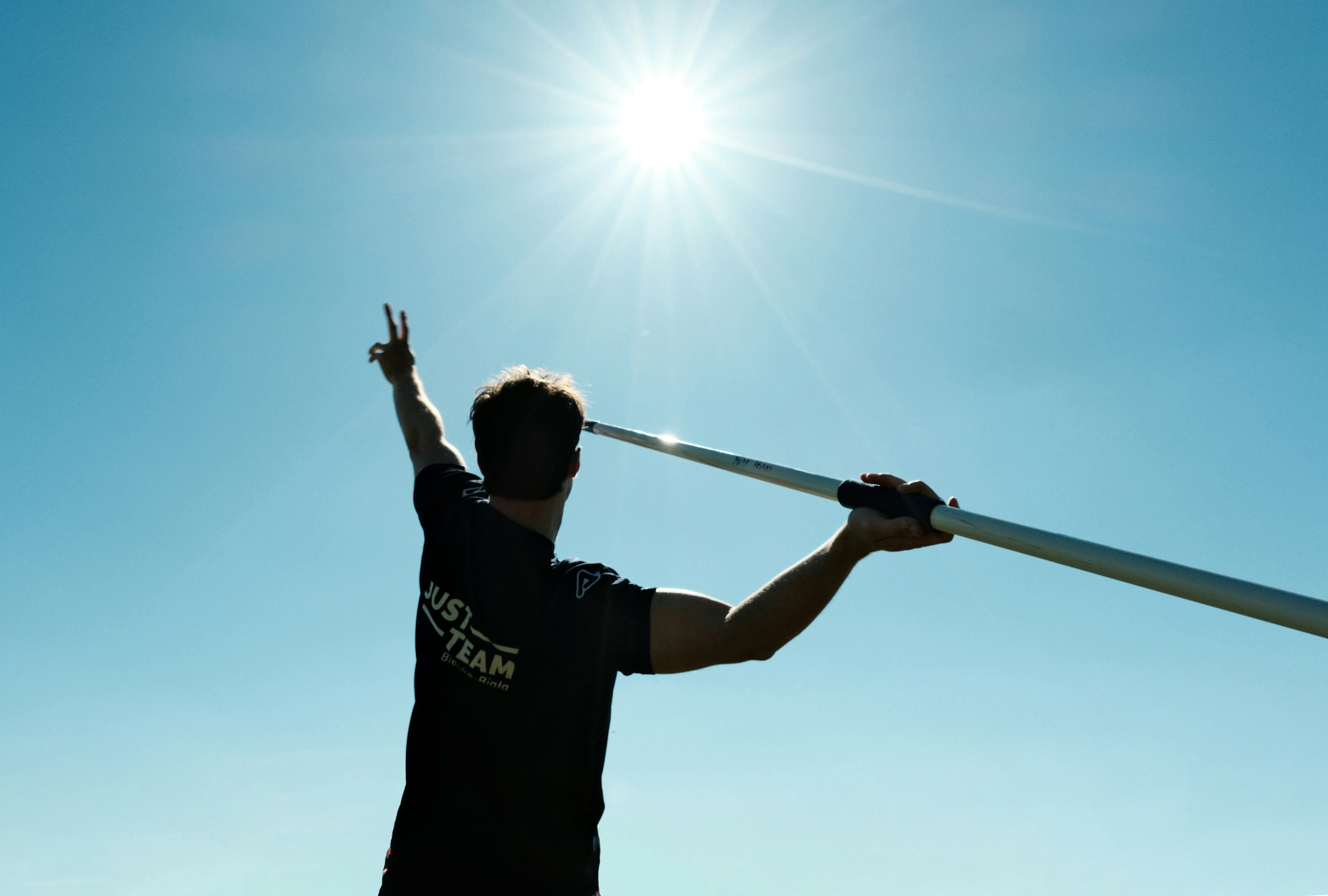 Una persona in controluce tiene un palo e fa un segno di pace.