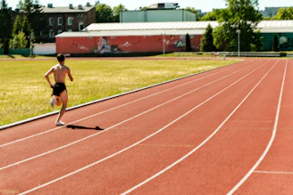 A shirtless man runs on a red athletic track.