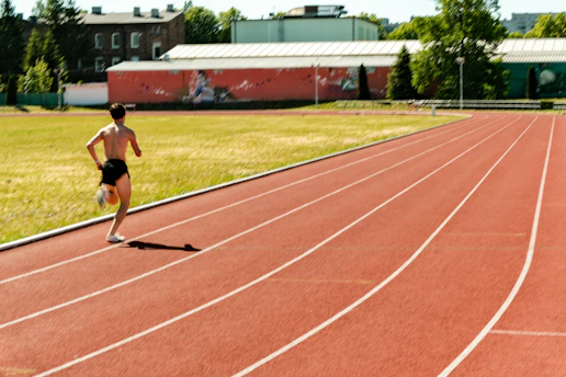 A shirtless man runs on a red athletic track.