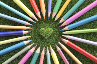 Colored pencils form a circle around a green grass heart.