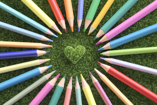 Colored pencils form a circle around a green grass heart.