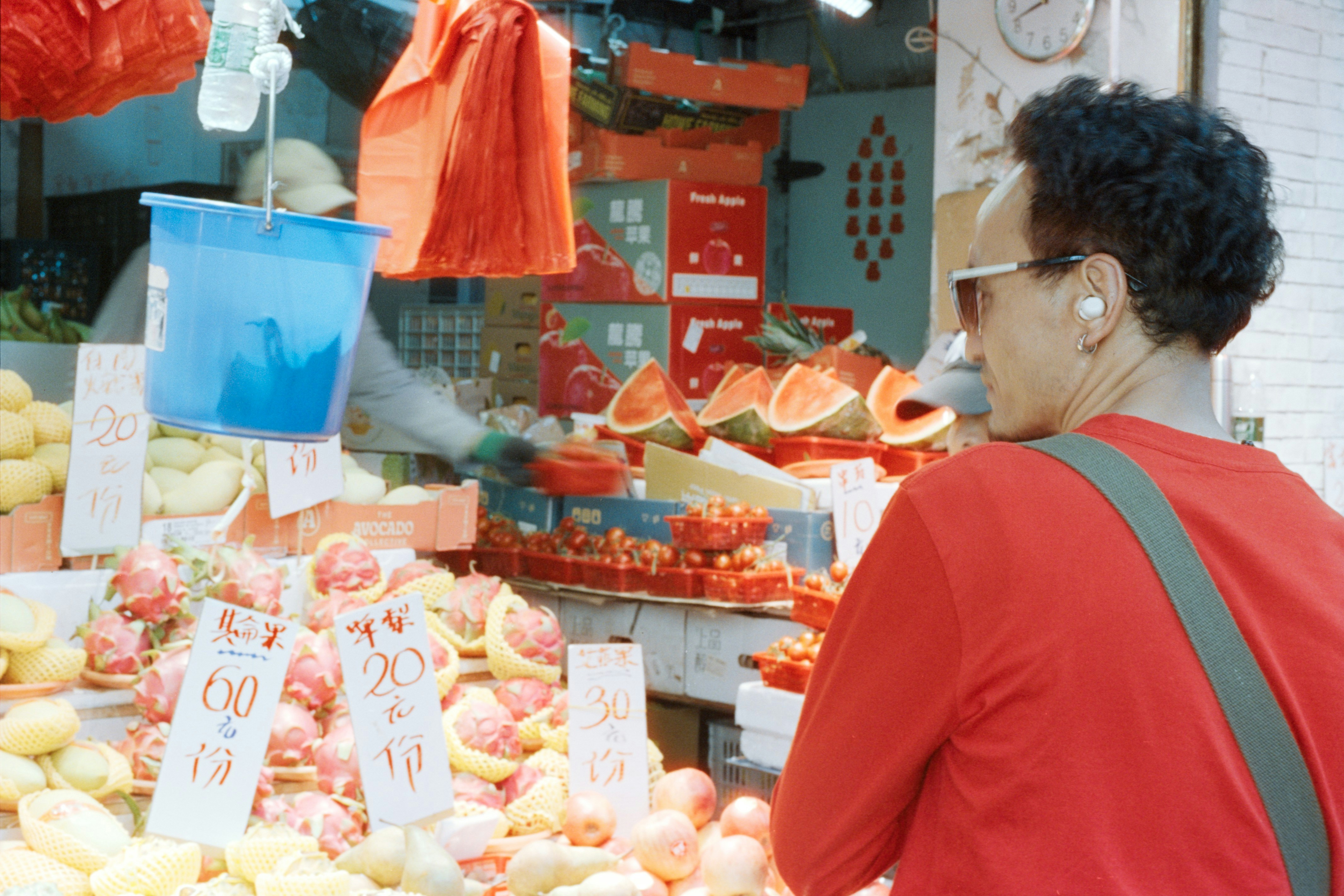 Shopper in a red shirt browsing a fruit stall