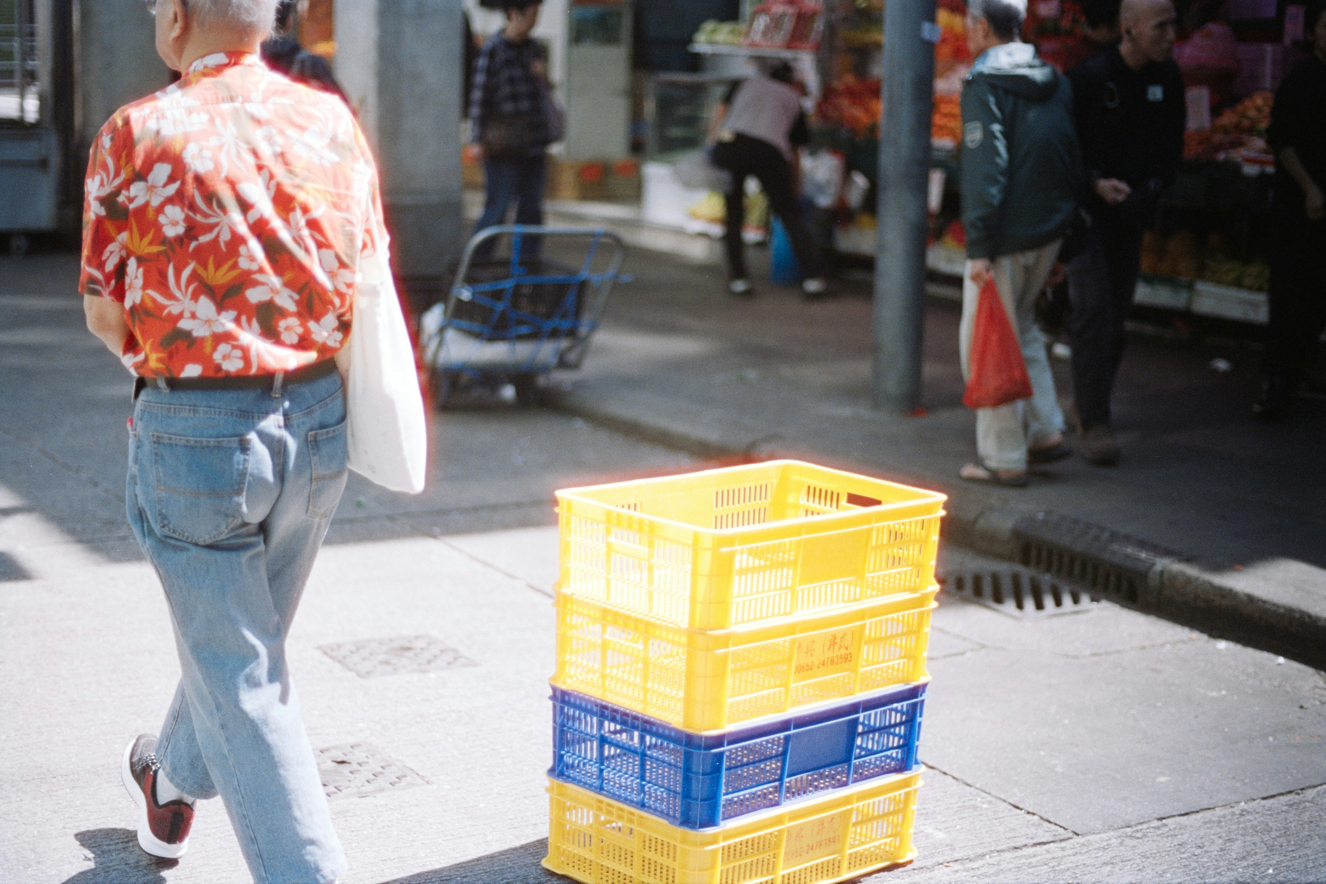 Person in floral shirt walks past stacked crates on sidewalk