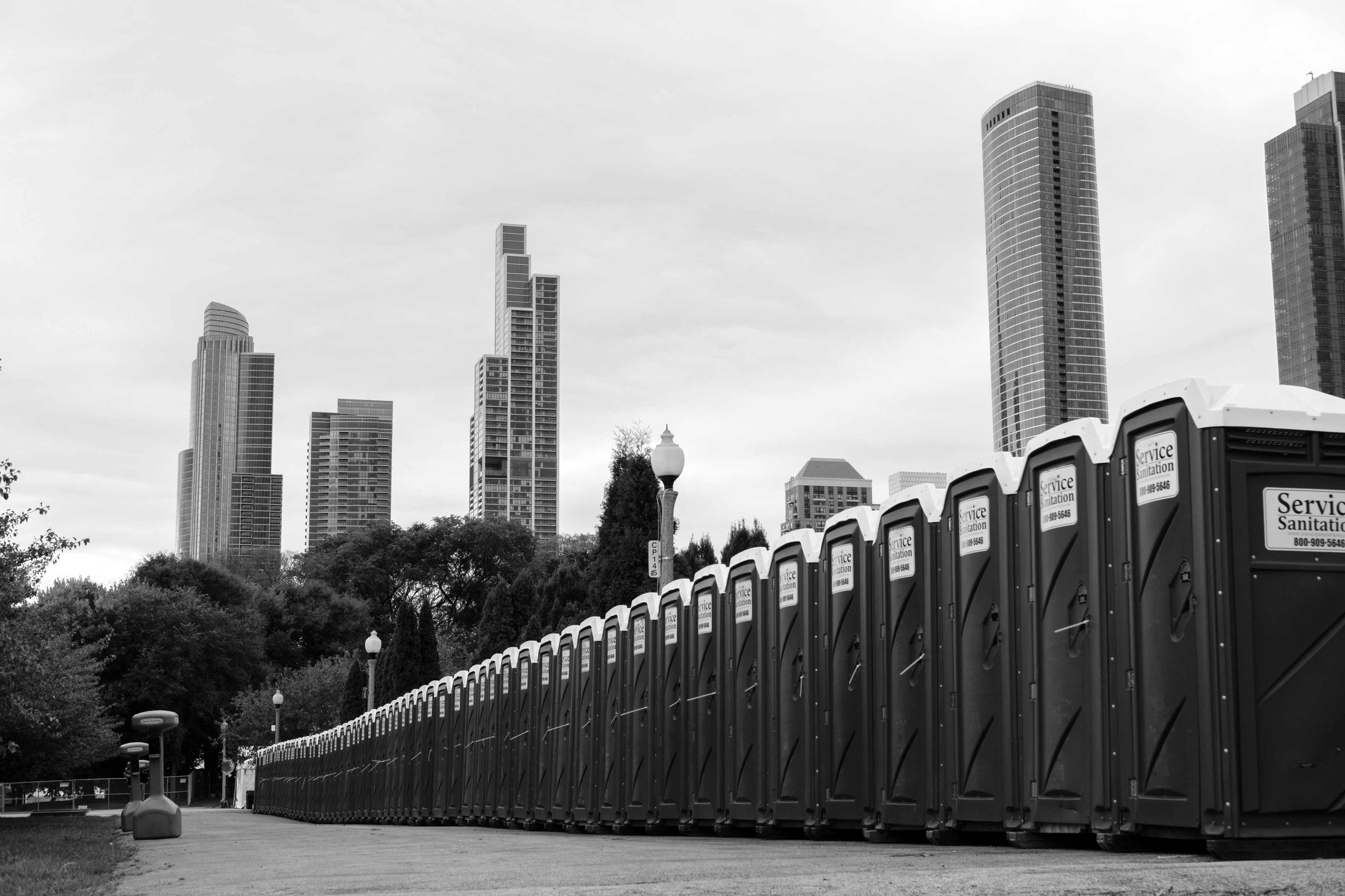 Long row of portable toilets with city skyscrapers in background.