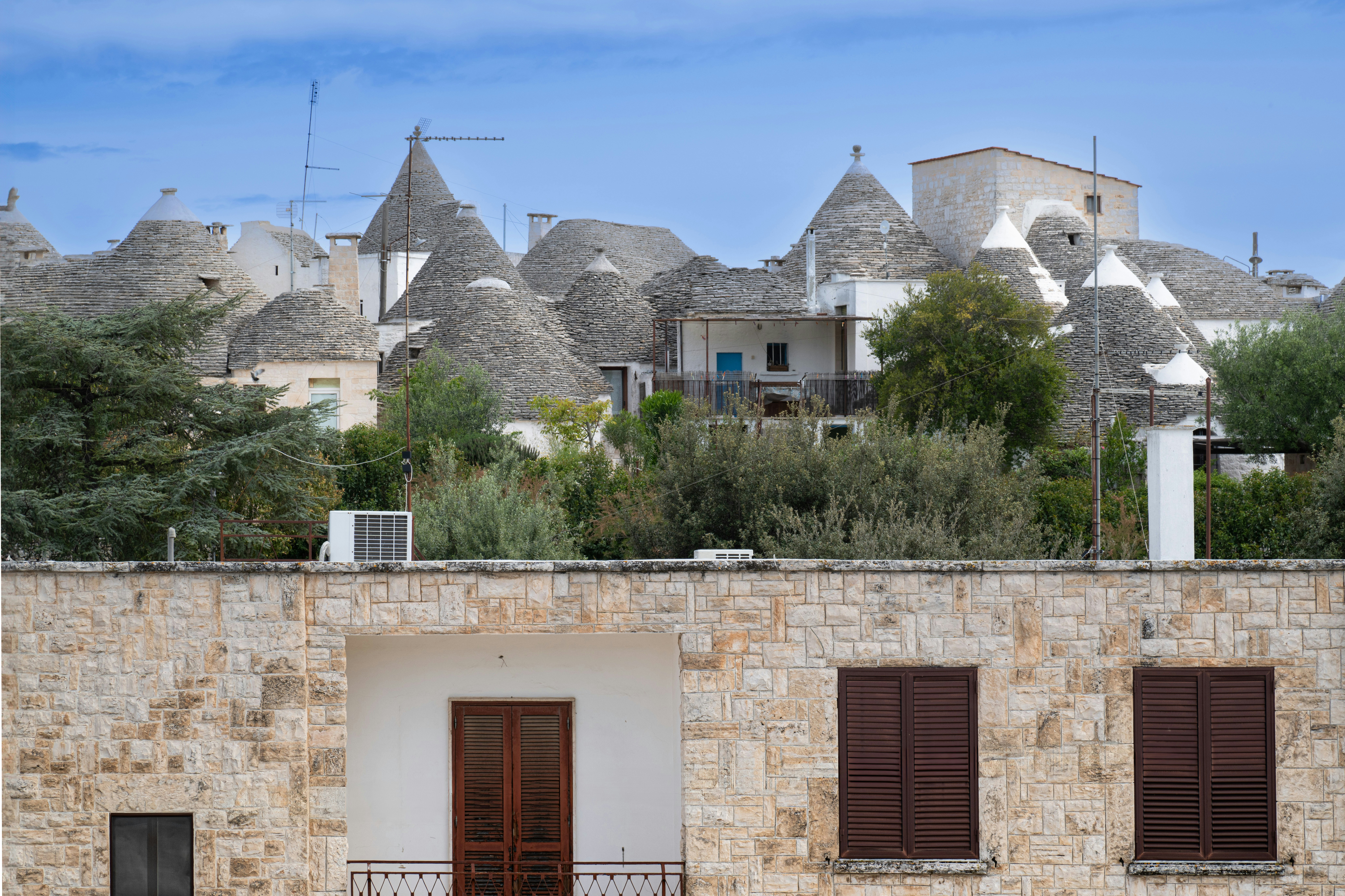 Casas tradicionais trulli com telhados cônicos atrás de um edifício de pedra.