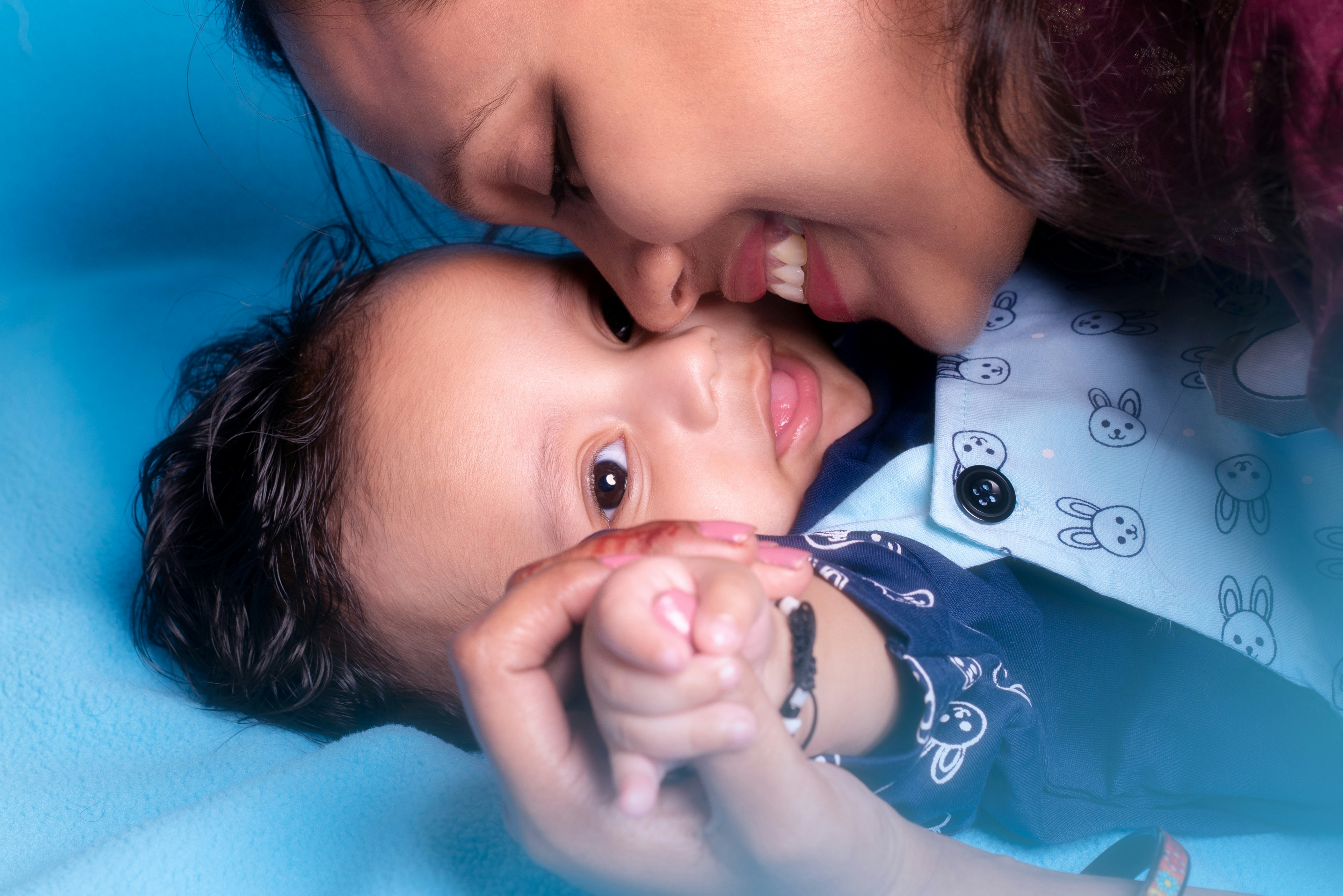 Wanita tersenyum dengan penuh kasih sayang mencium pipi bayi dengan latar belakang biru