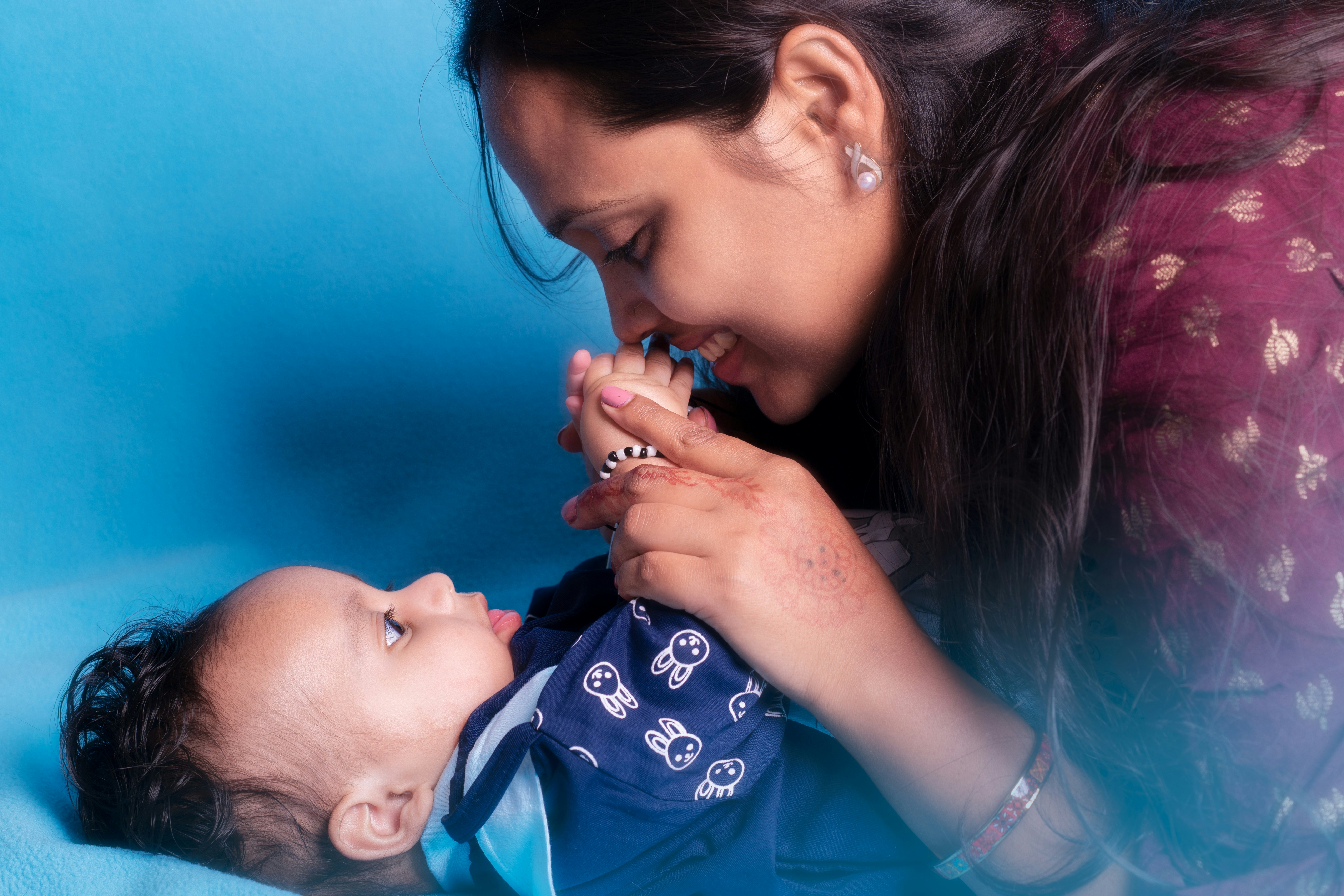 Ibu dengan lembut memegang kaki bayi dengan latar belakang biru.