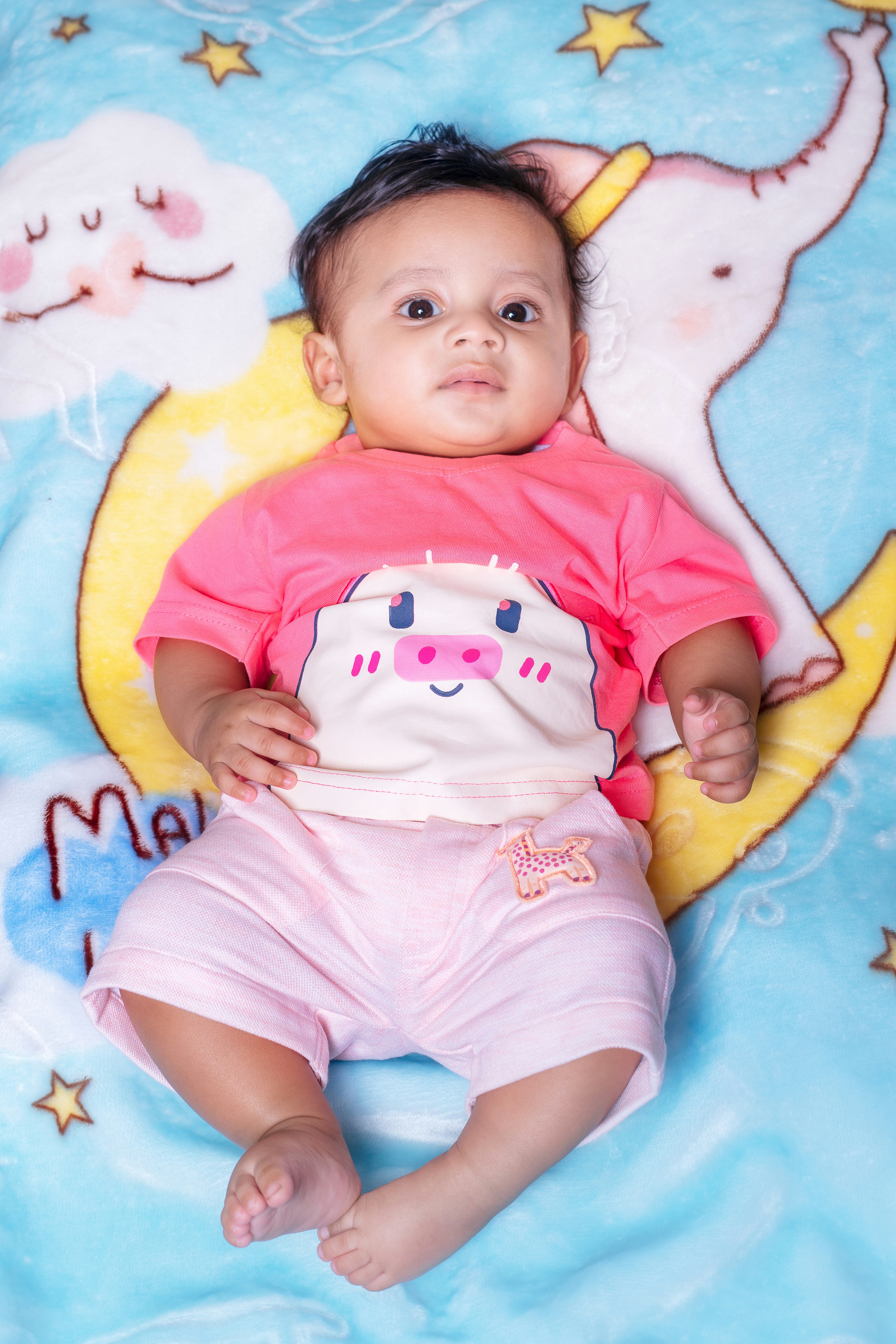 Bayi lucu dengan pakaian merah muda di atas selimut biru bermotif.
