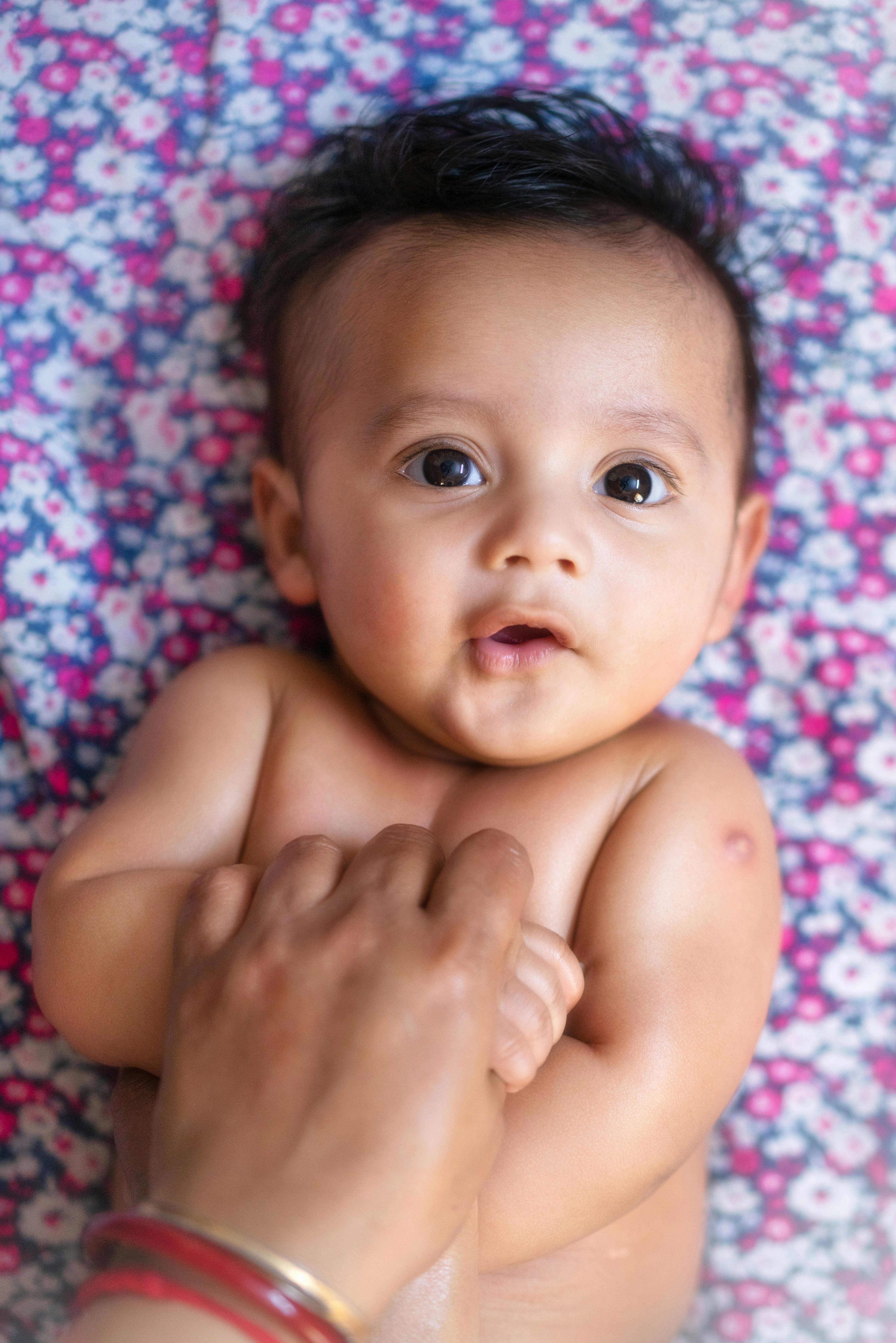 Cute baby looking up, held by an adult hand.