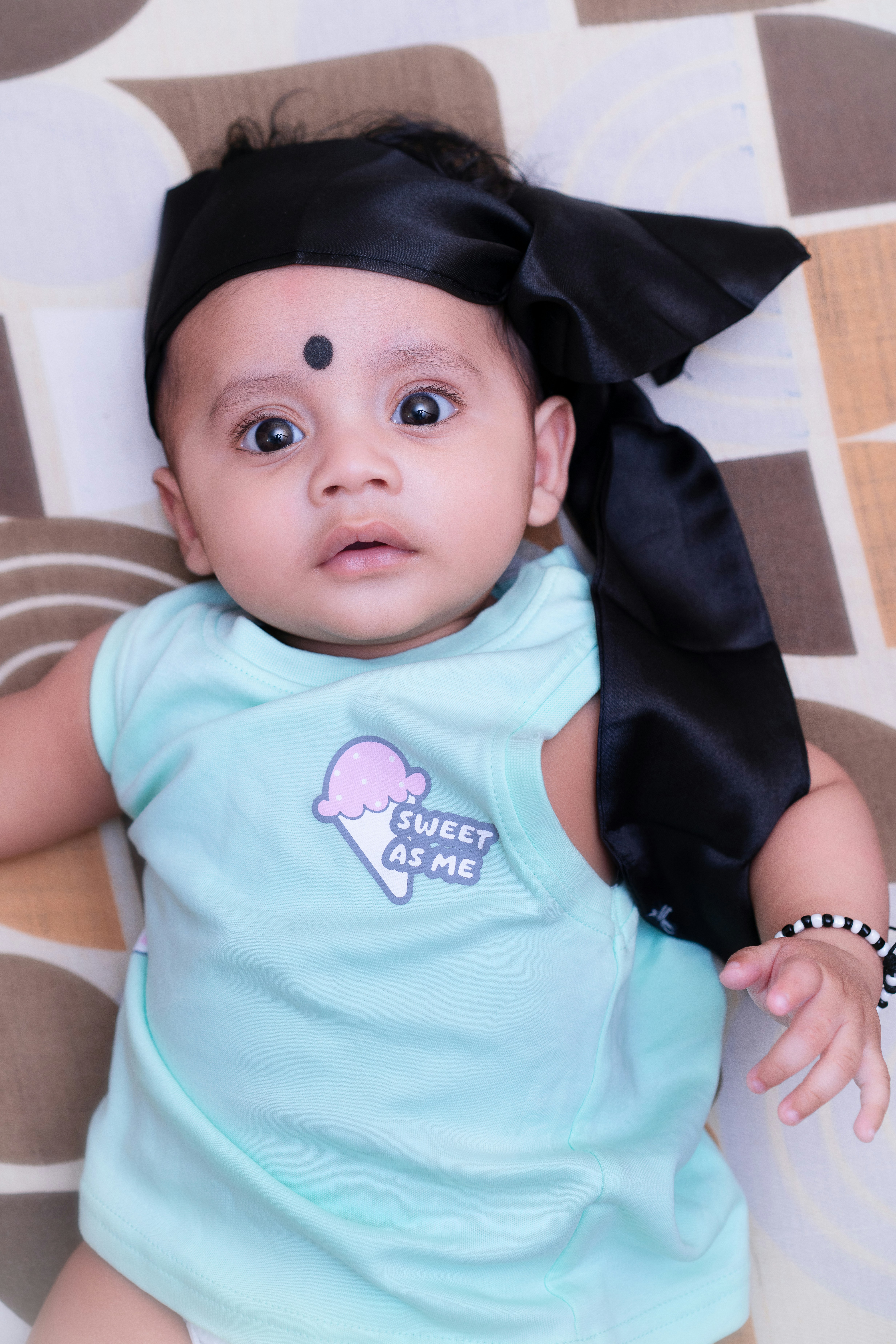 Adorable baby with a black headscarf and bindi looking up.