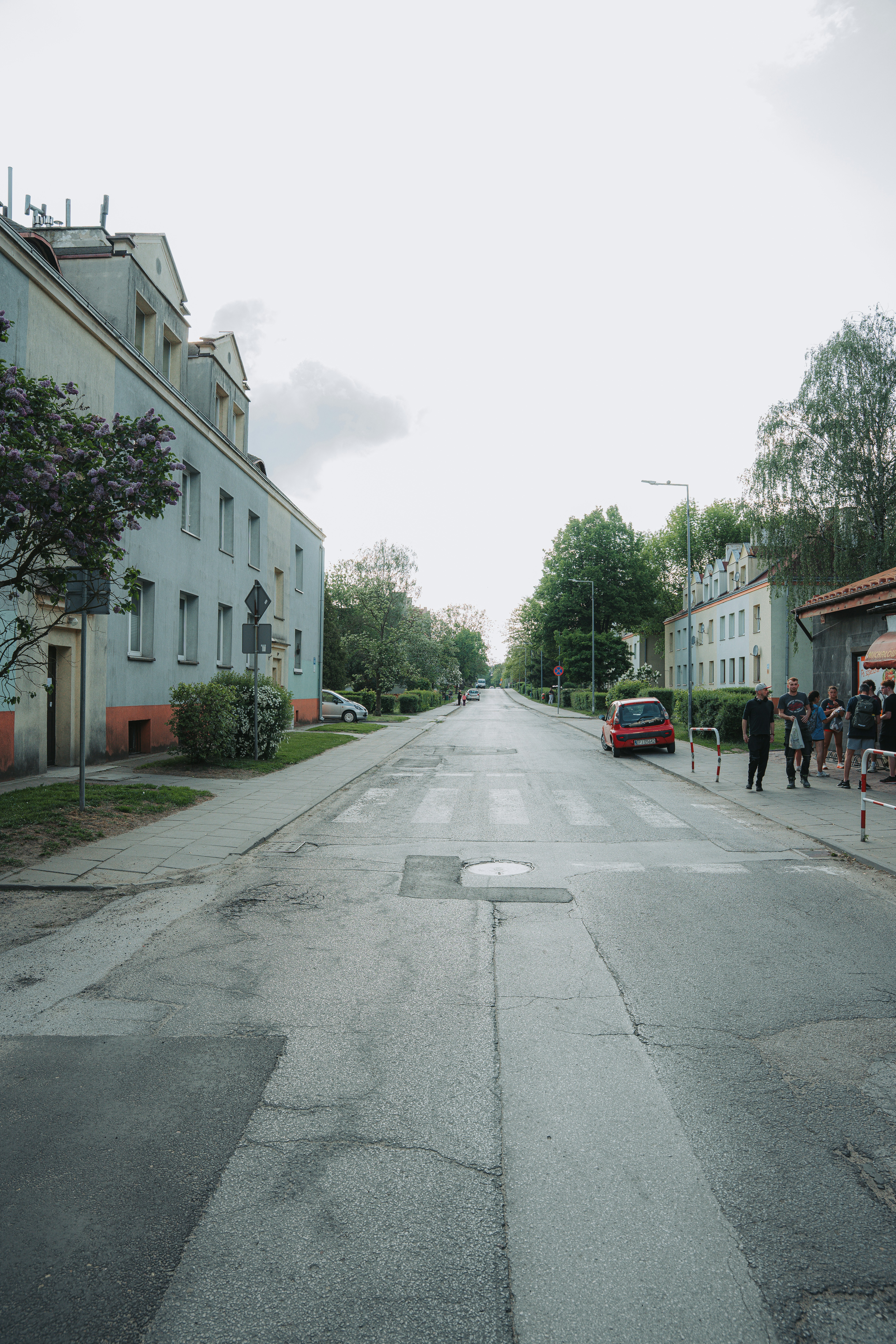Stadtstraße mit Gebäuden, Bäumen, geparktem Auto und Fußgängern