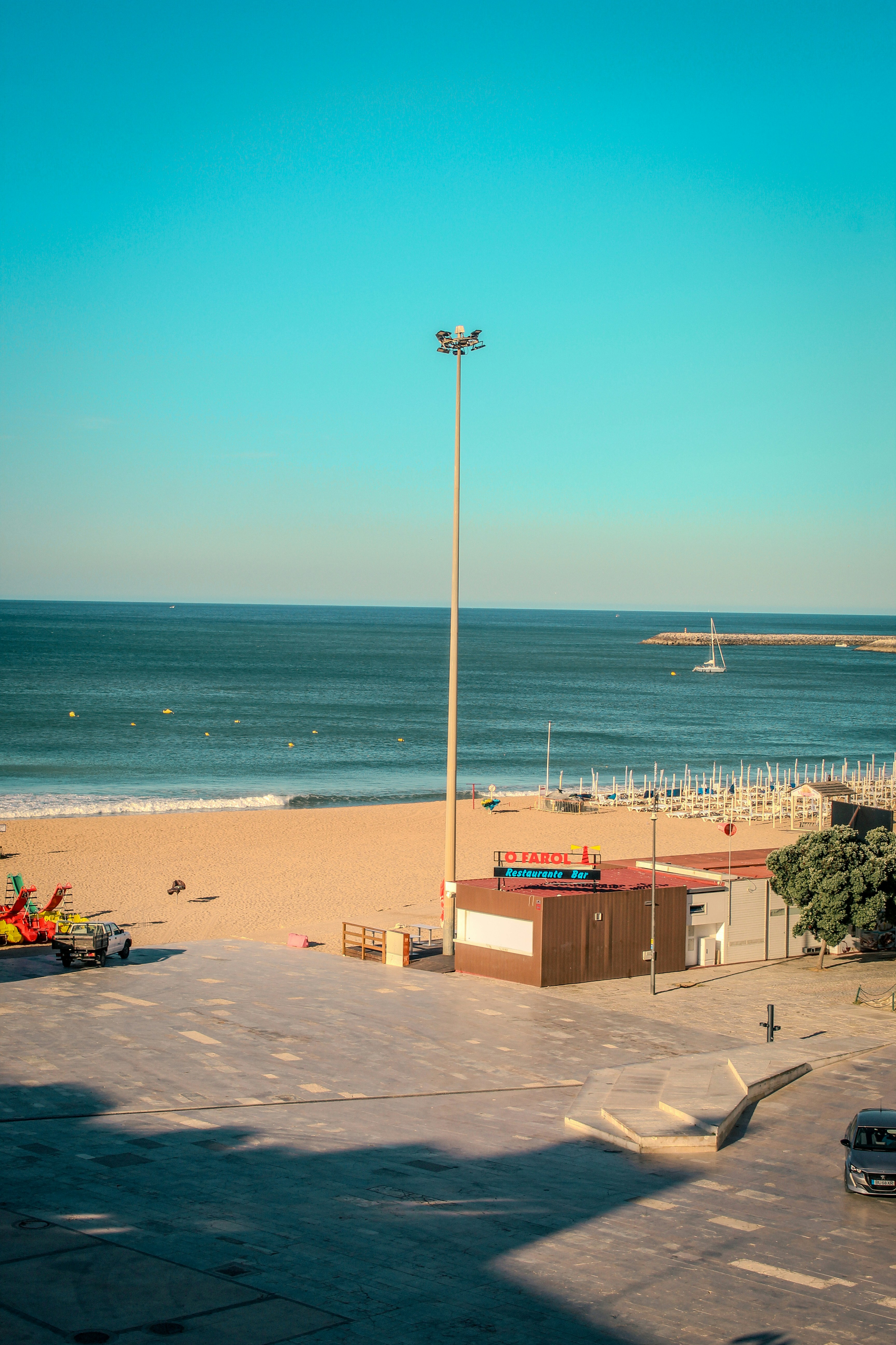 Sunny beach with a tall lamppost, building, and blue ocean.