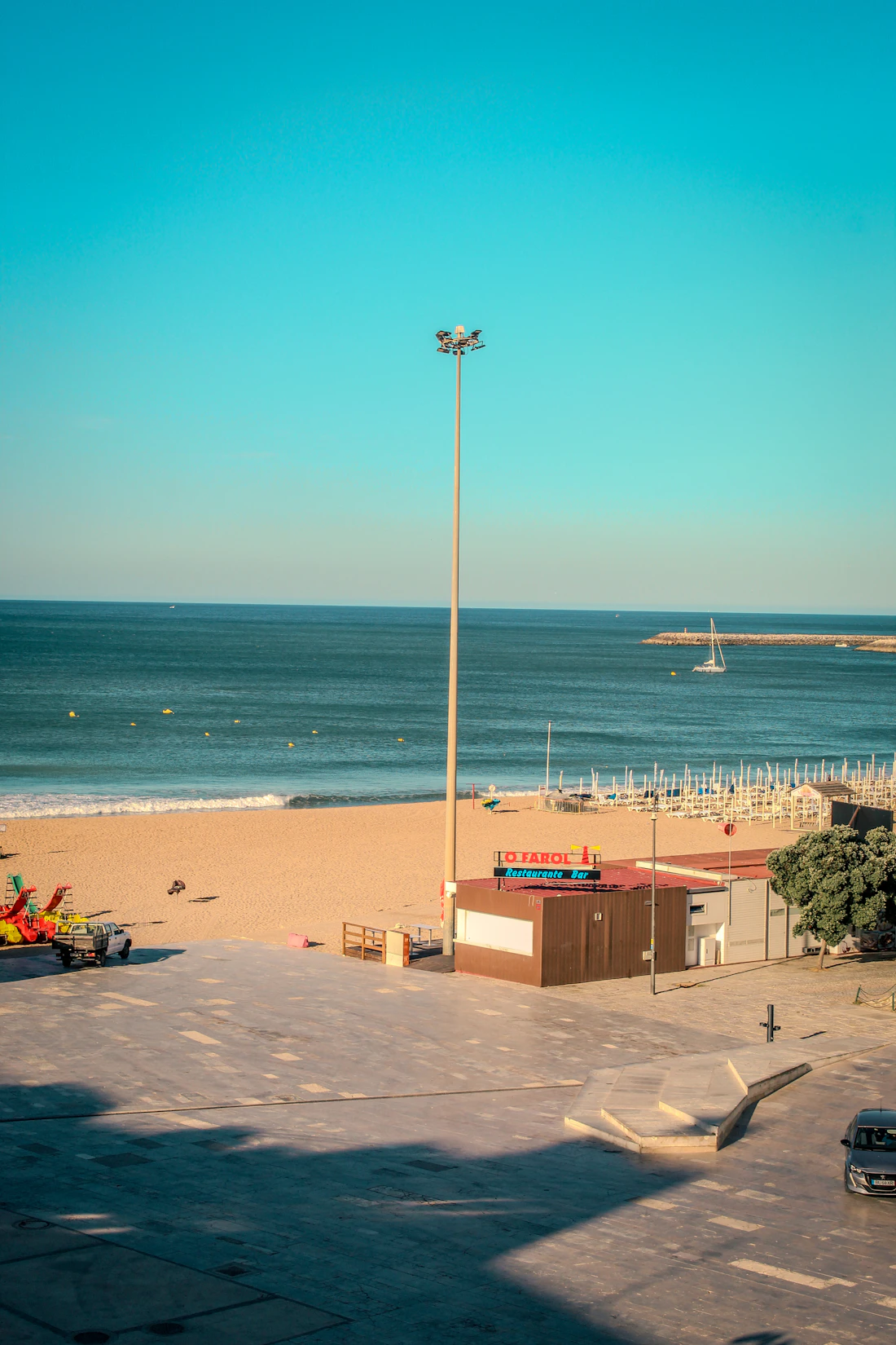 Sunny beach with a tall lamppost and a blue ocean