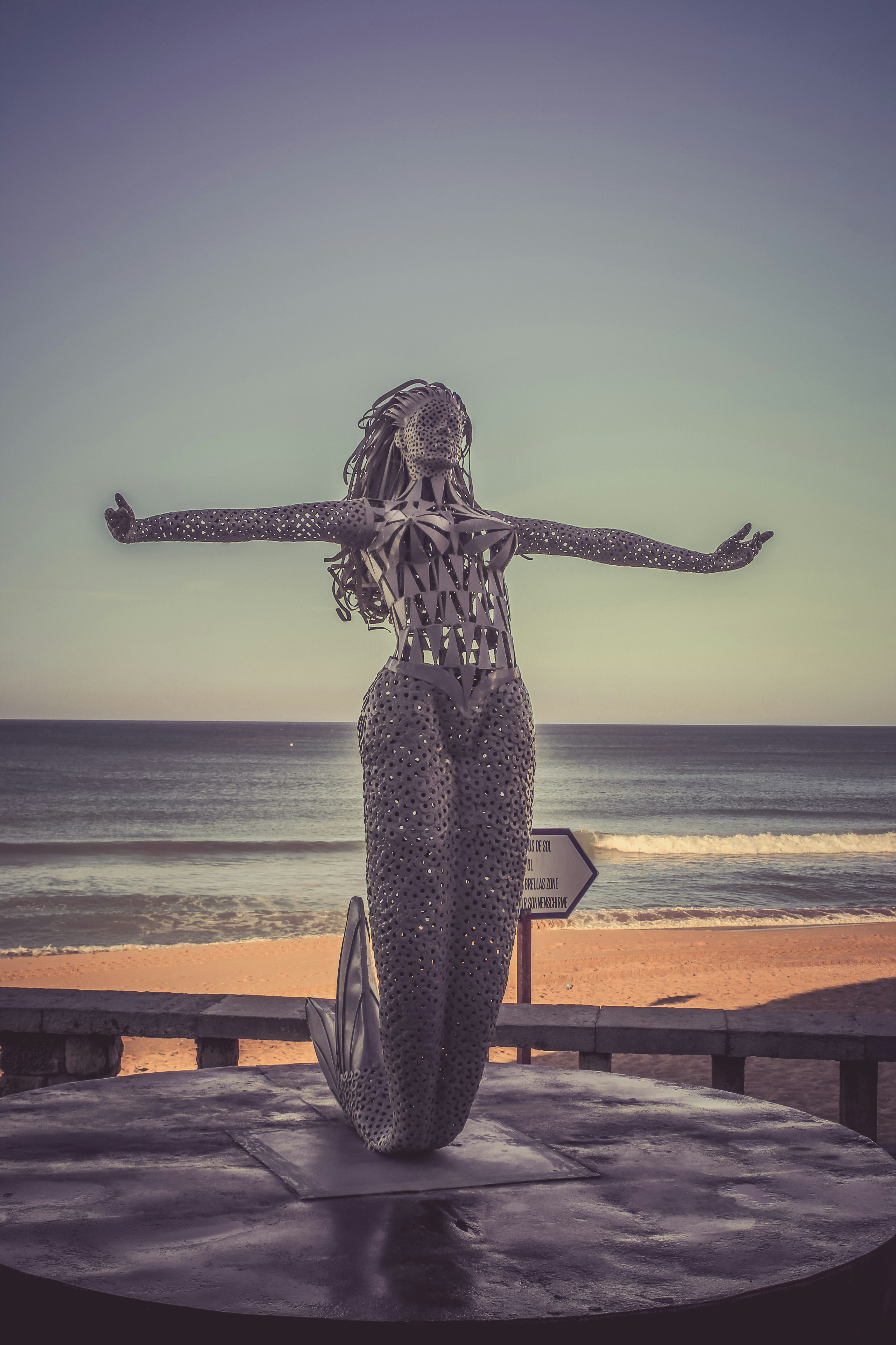 A mermaid statue stands on a platform overlooking the ocean.