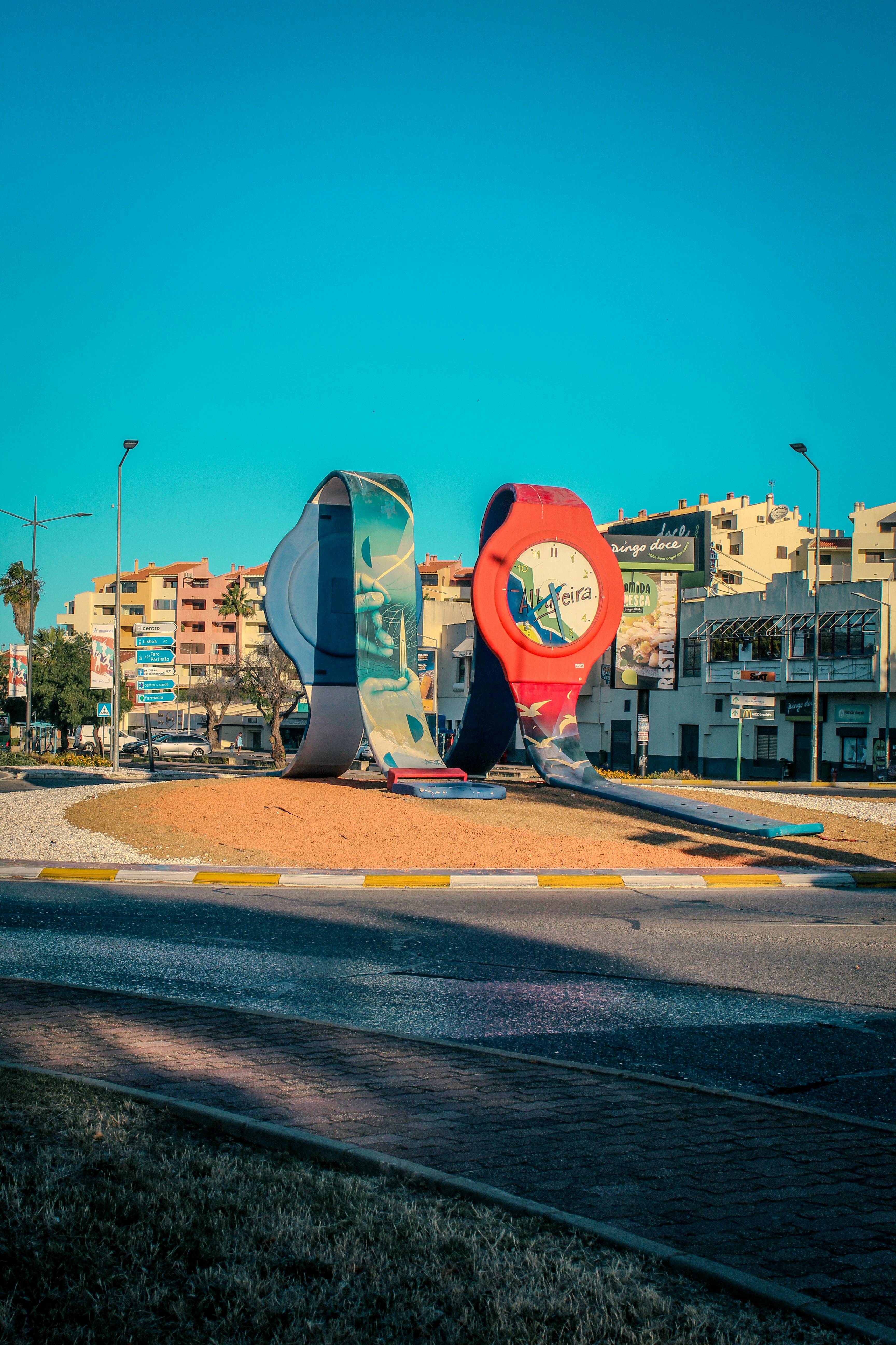 Colorful watch sculptures adorn a roundabout in a sunny town.