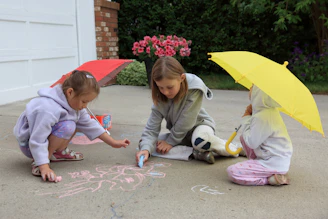 Children drawing on pavement with chalk under colorful umbrellas