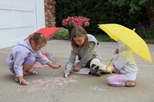 Children drawing on pavement with chalk under colorful umbrellas