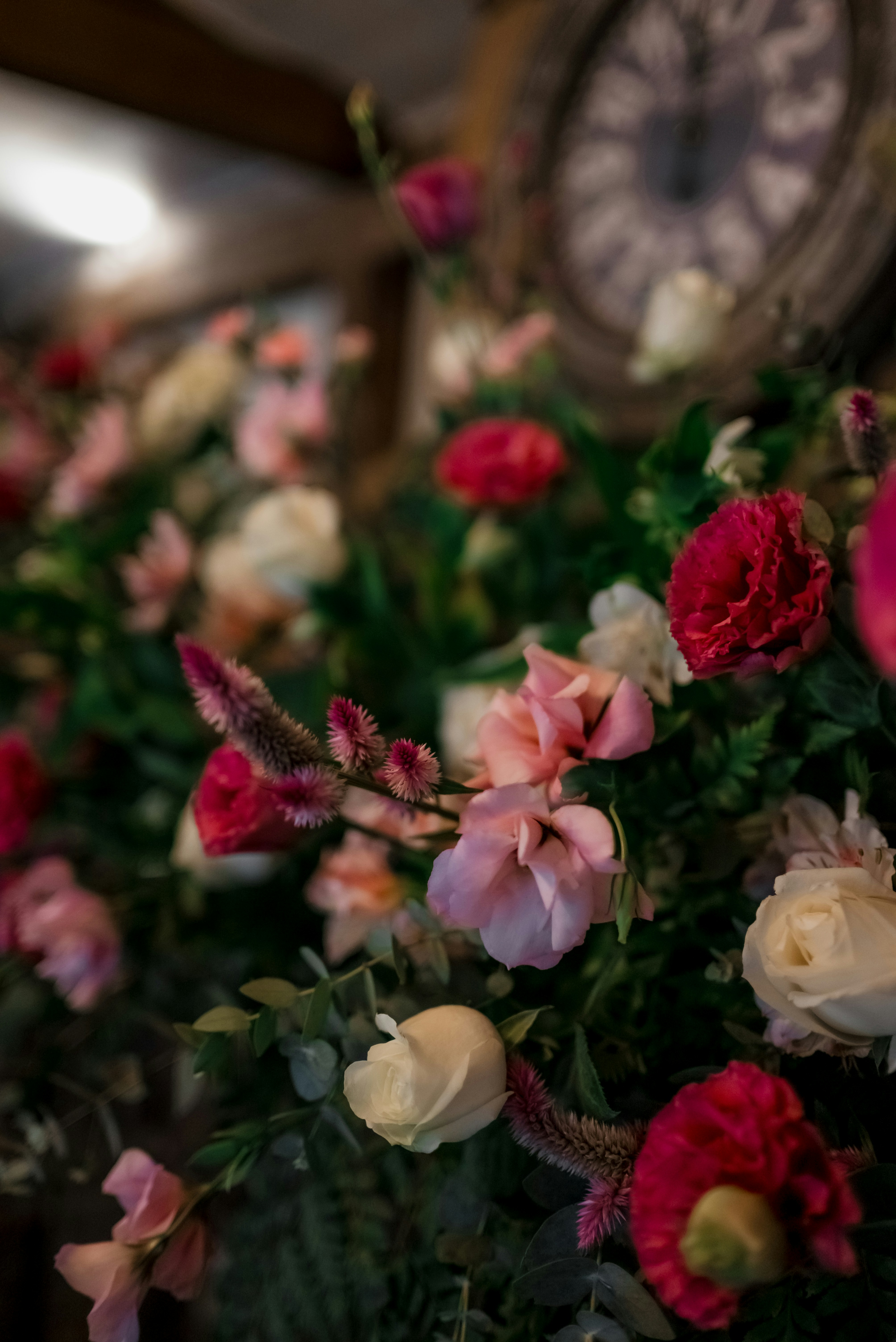 Bunte rosa, rote und weiße Blumen mit einer verschwommenen Uhr.