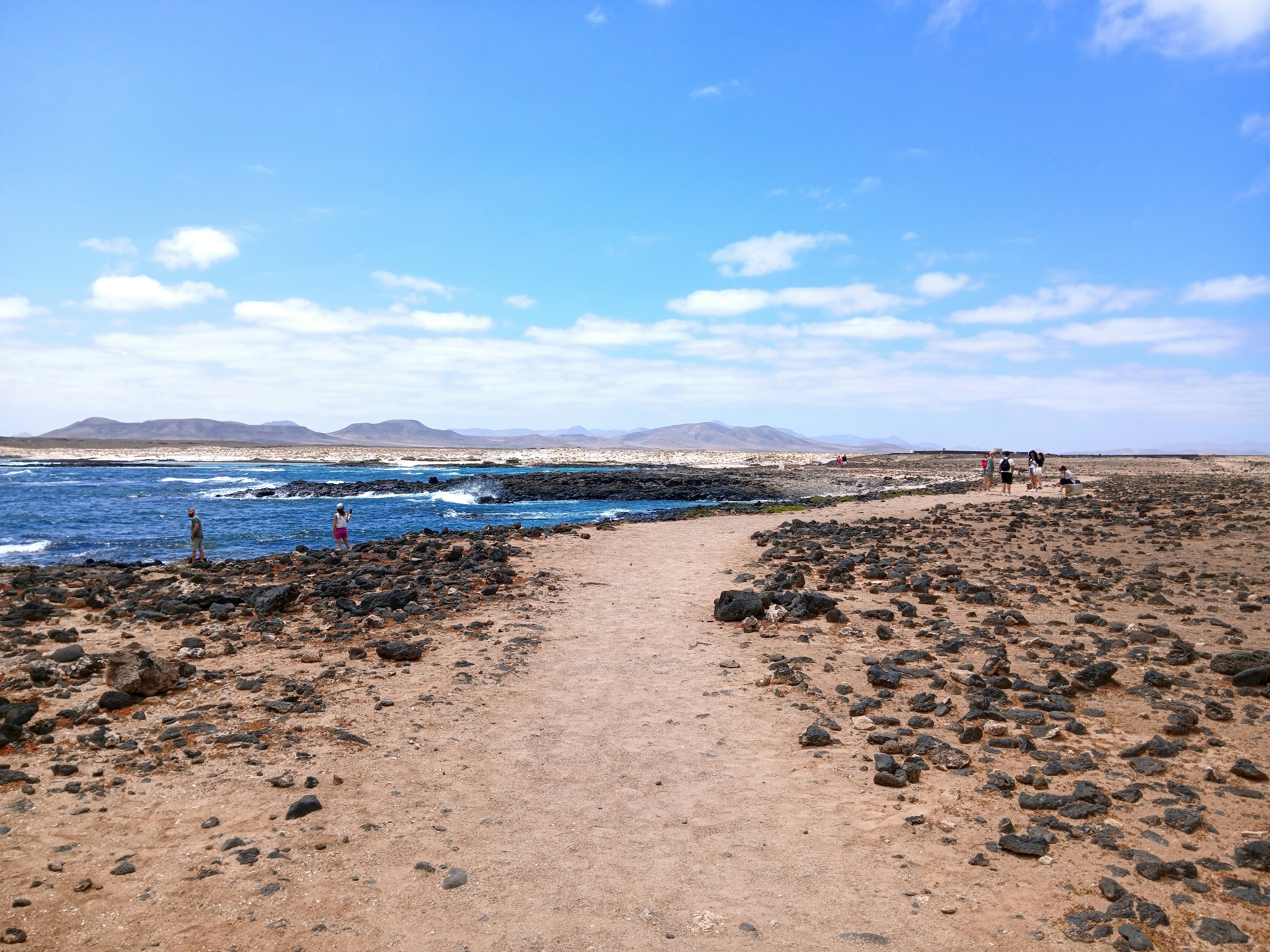 Path through volcanic landscape towards ocean and distant hills