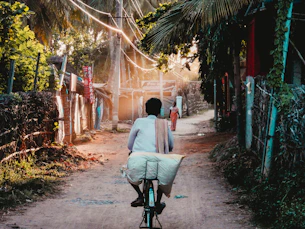 Man on bicycle riding down a sunny village path