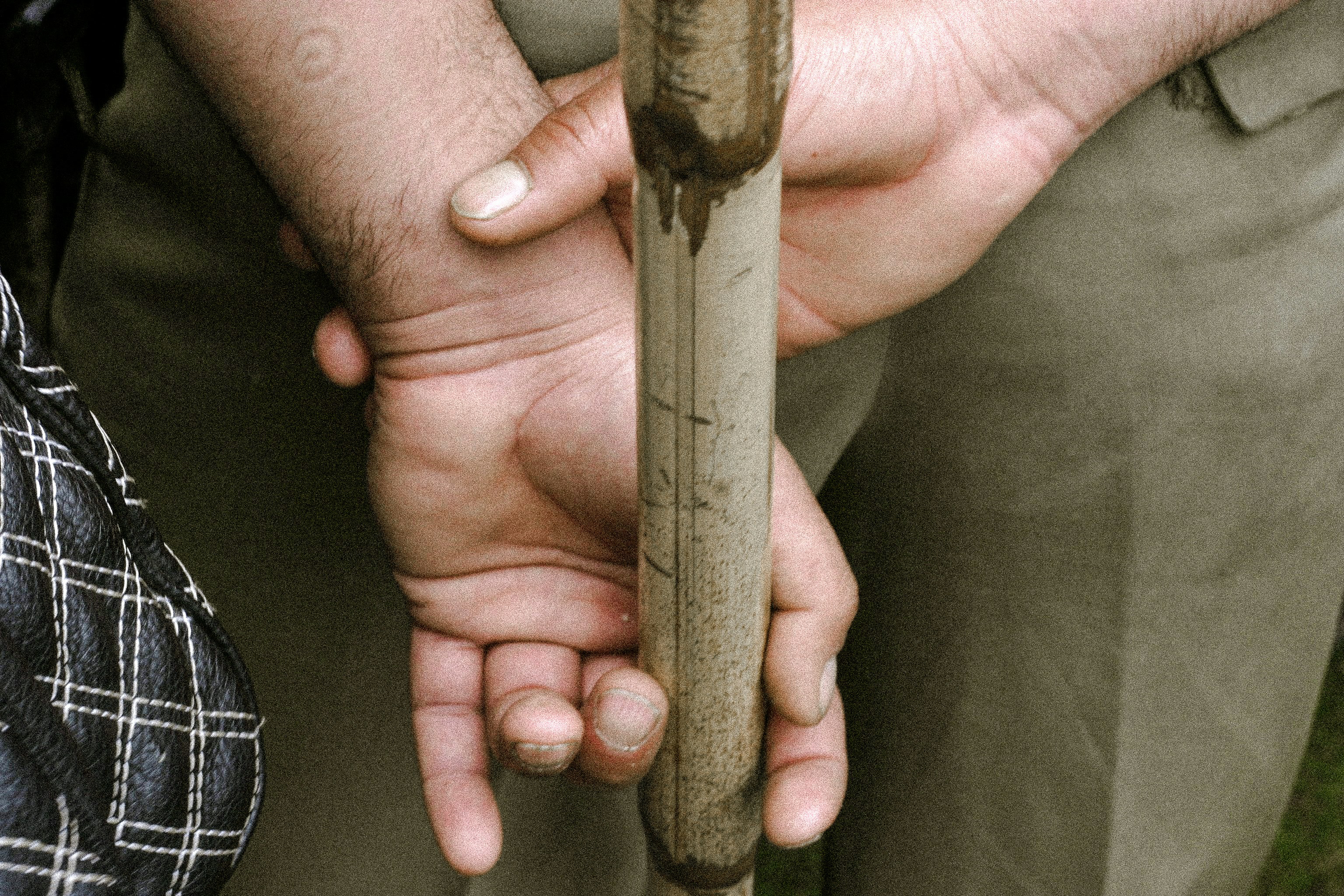 Hands clasped behind back holding a dirty wooden stick.