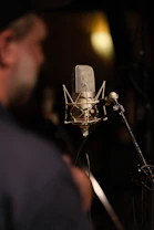 Vintage studio microphone with a musician in the background.