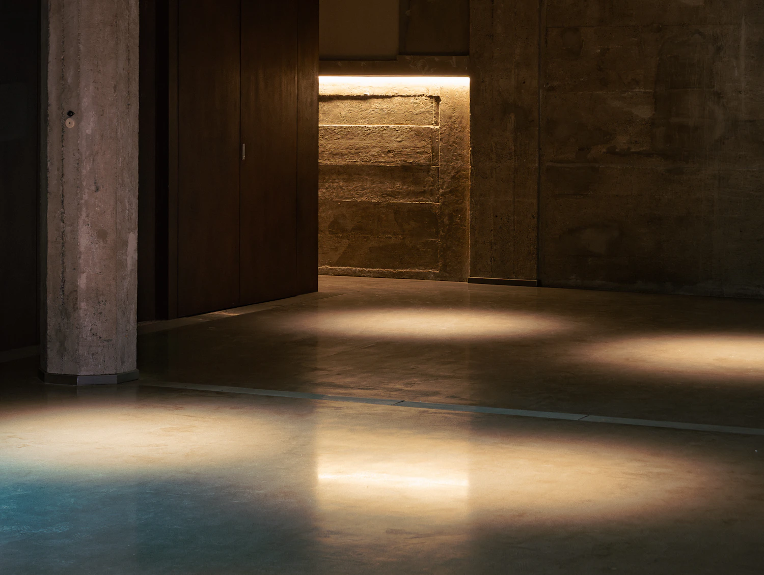 A dark concrete room with light arriving from an open doorway at the far end