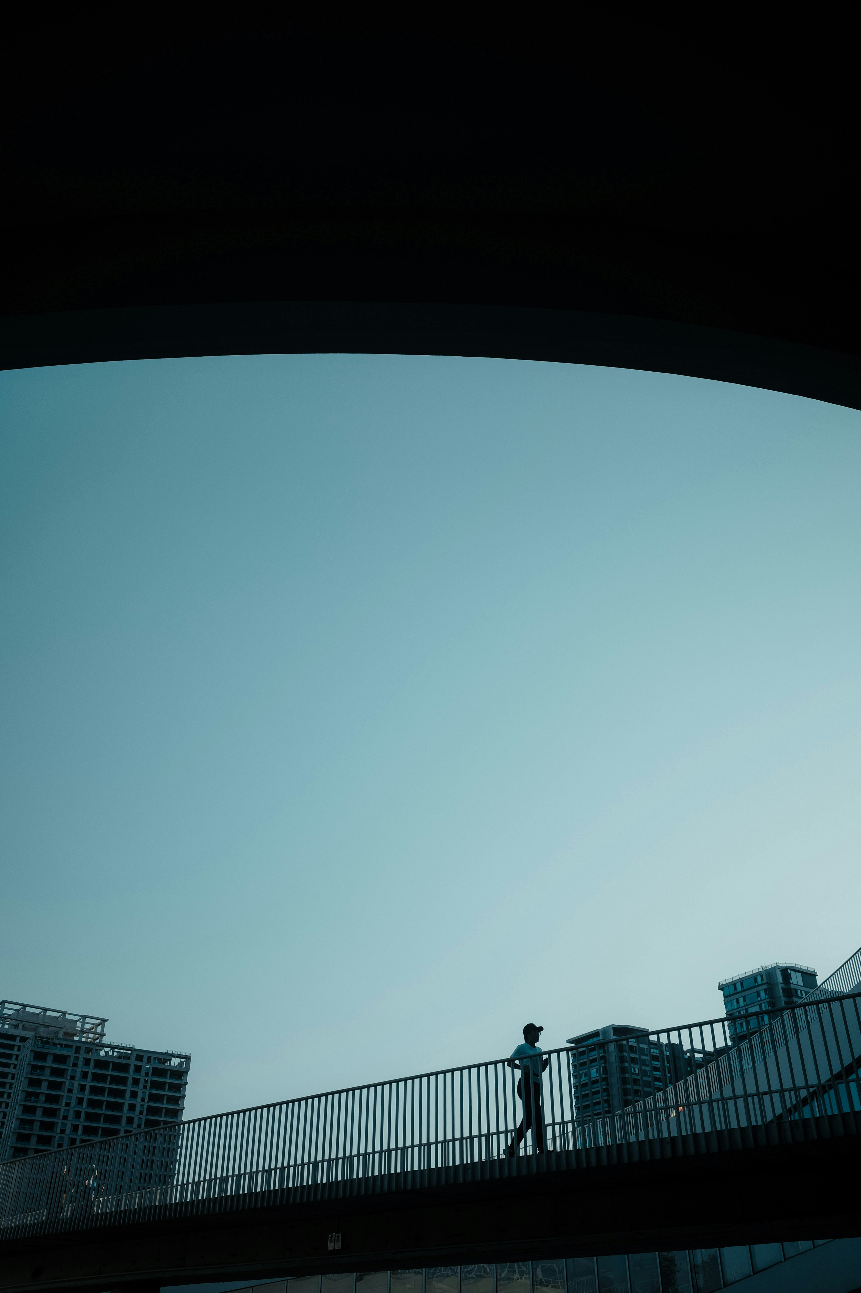 Silhouetted person walks on a bridge under a clear sky.