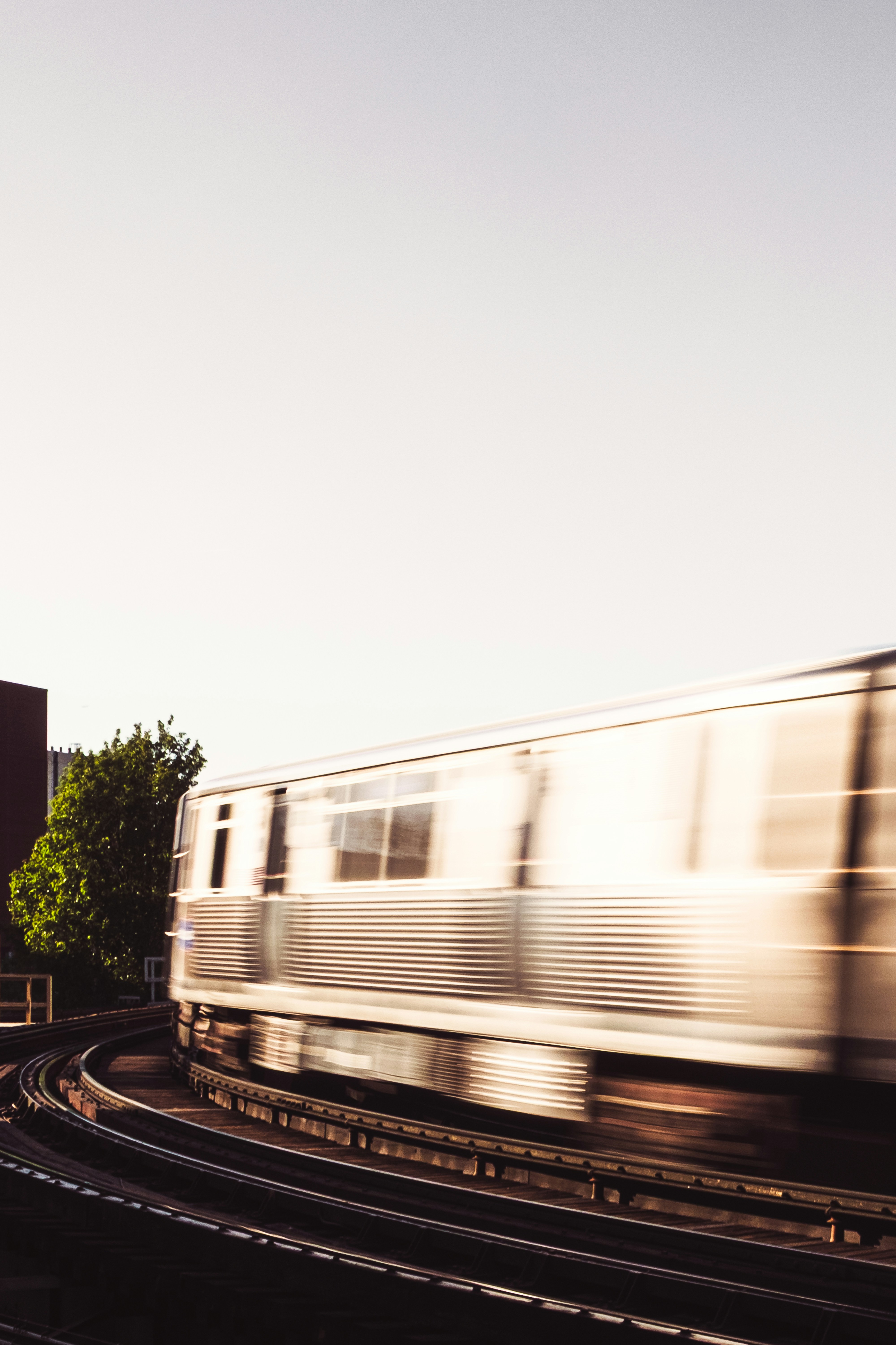 Un tren borroso avanza a toda velocidad por vías elevadas al atardecer.