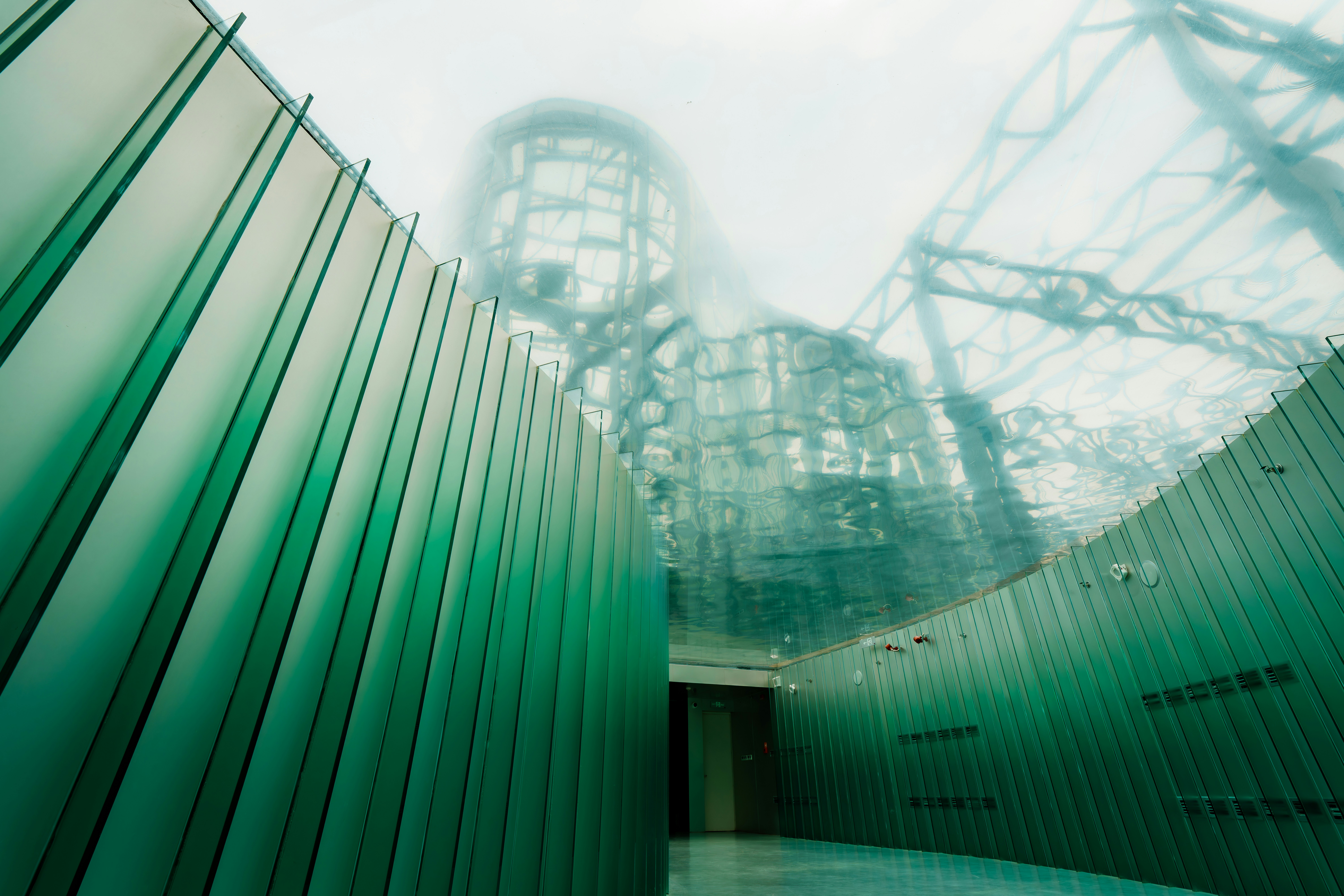 Green modern corridor leading to a large glass structure.