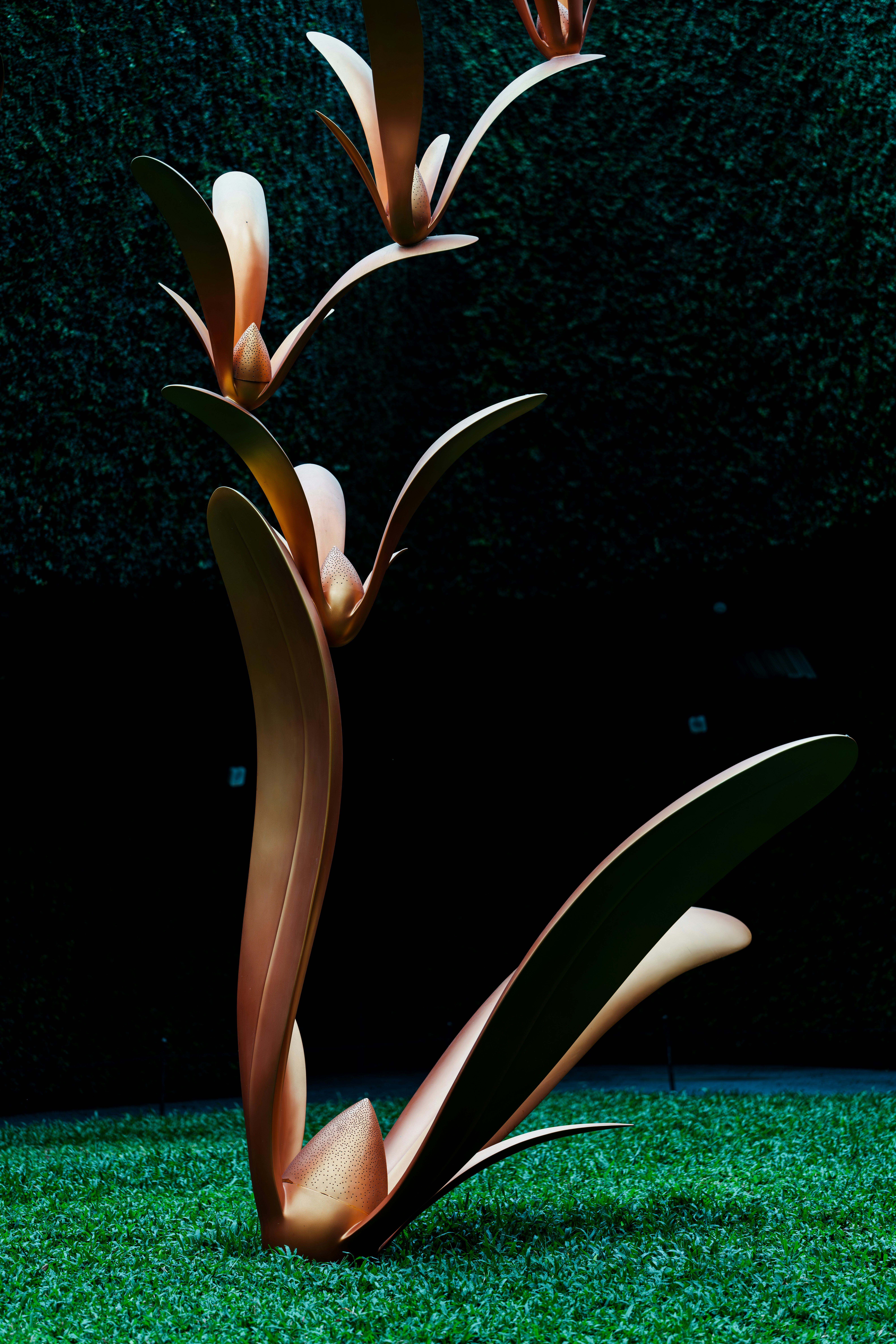 緑の草の上に金属製の植物のような彫刻があり、暗い背景に