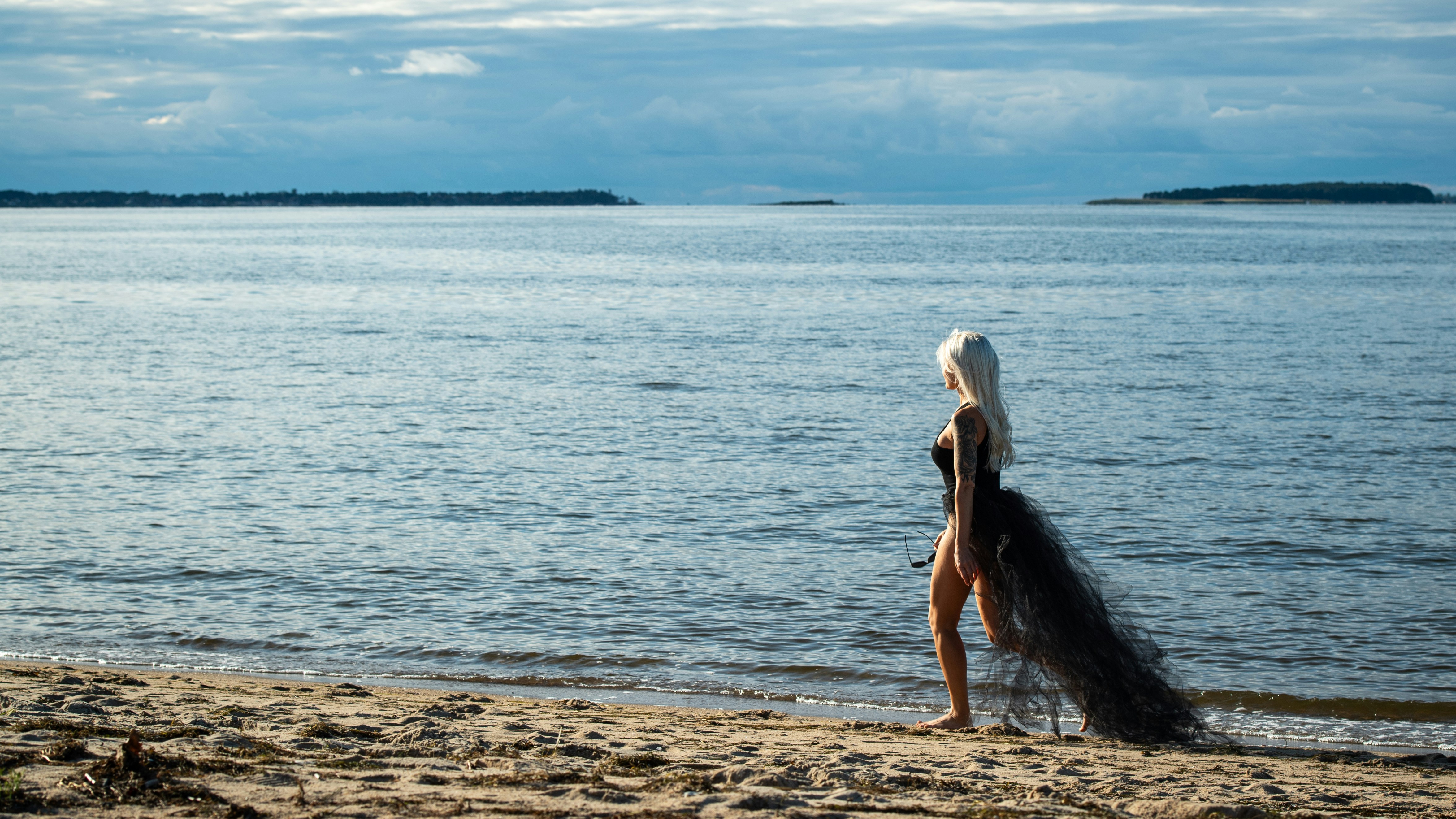 Blonde woman walks on sandy beach near calm ocean