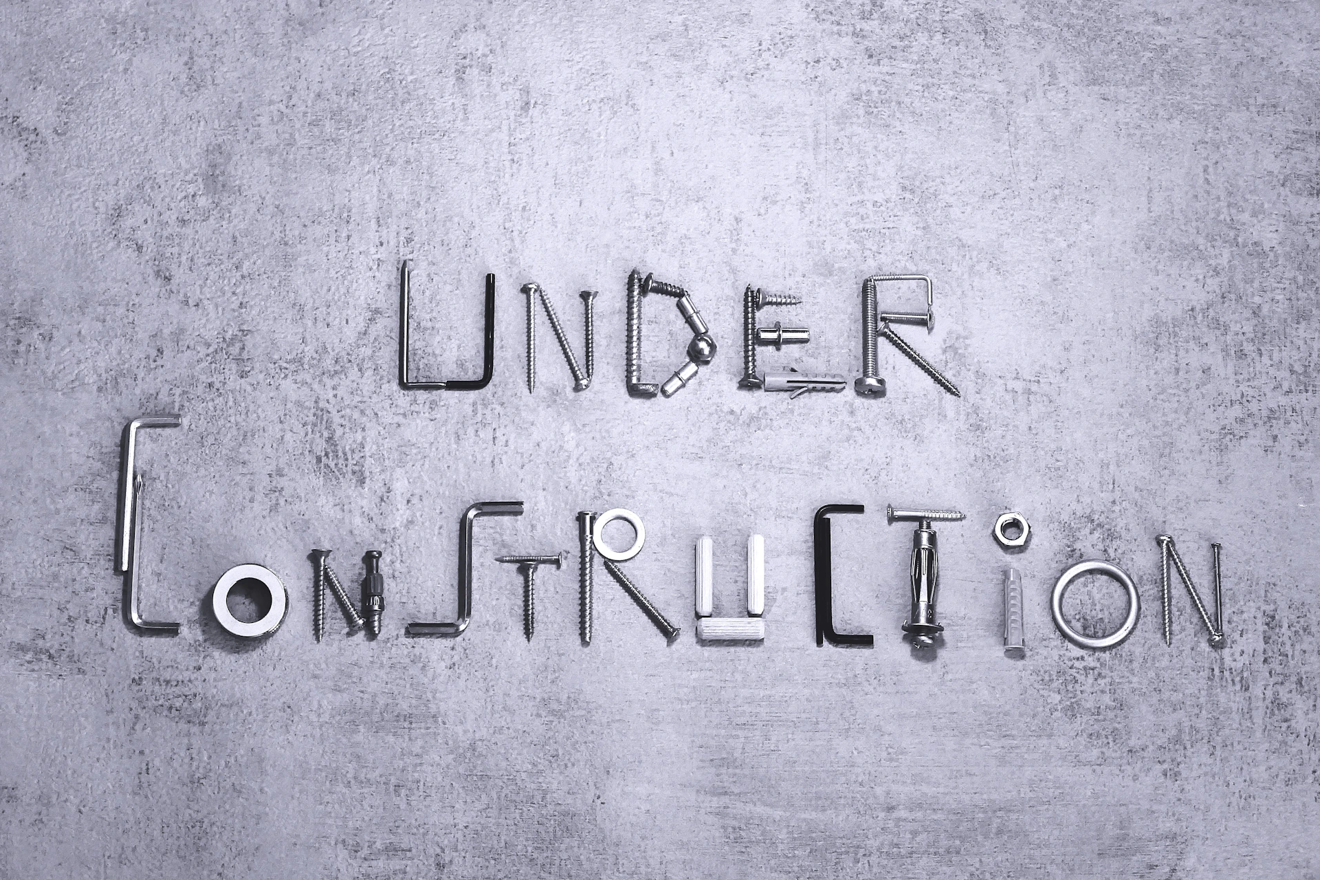 Under construction spelled with metal hardware on a gray background.