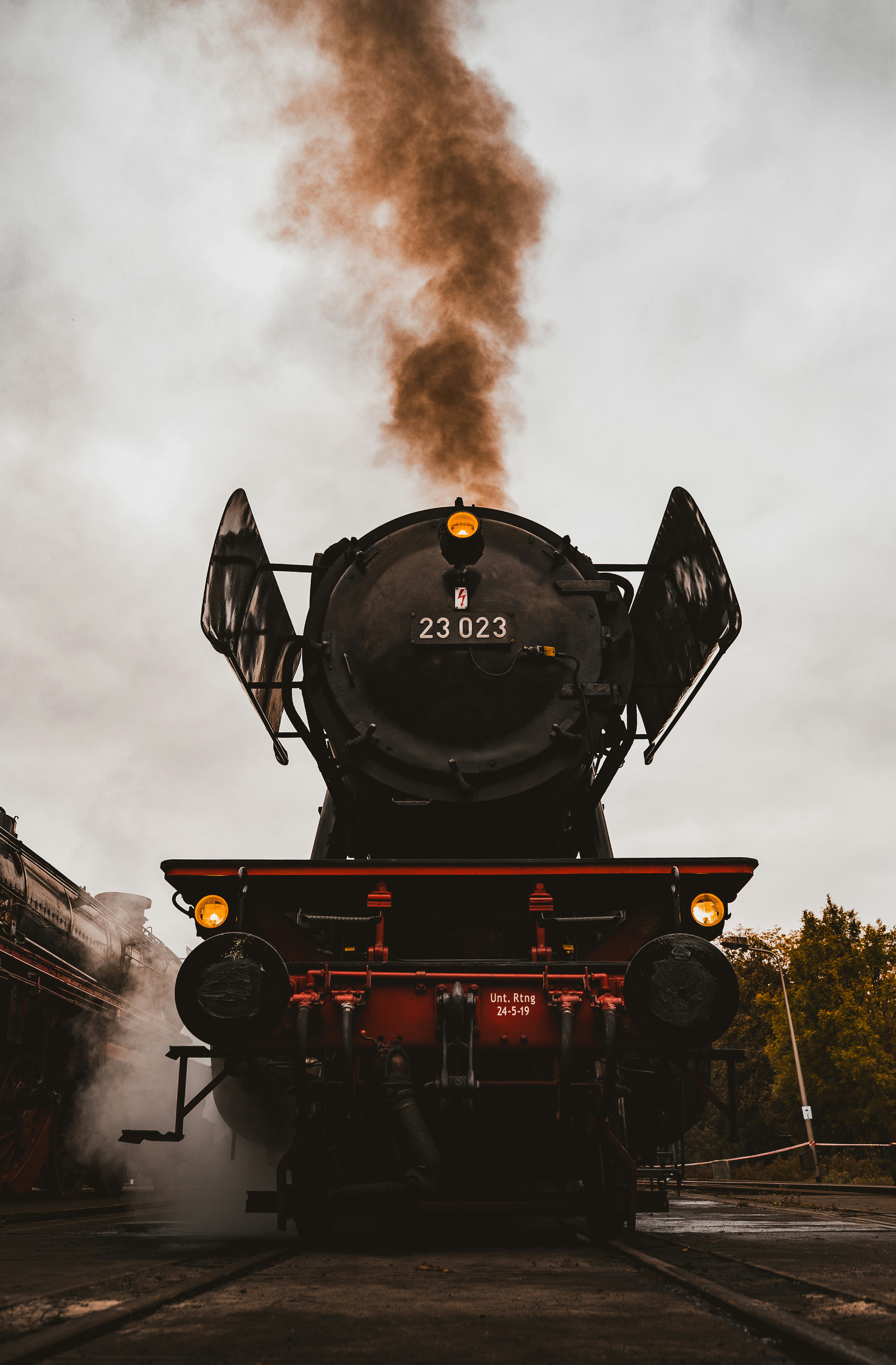 Una locomotora de vapor negra emitiendo humo bajo un cielo nublado.